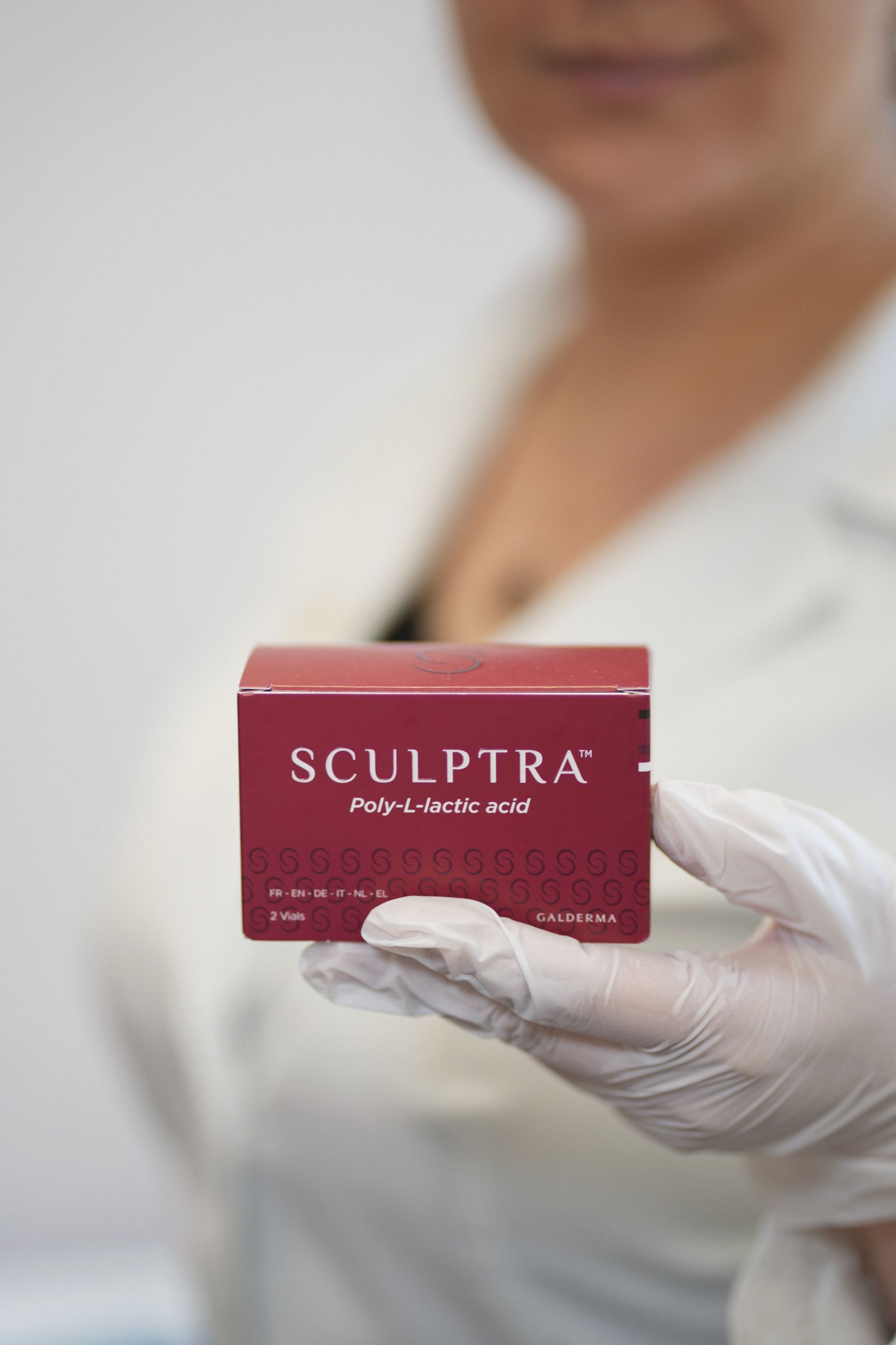 A woman wearing white gloves is holding a box of sculptra