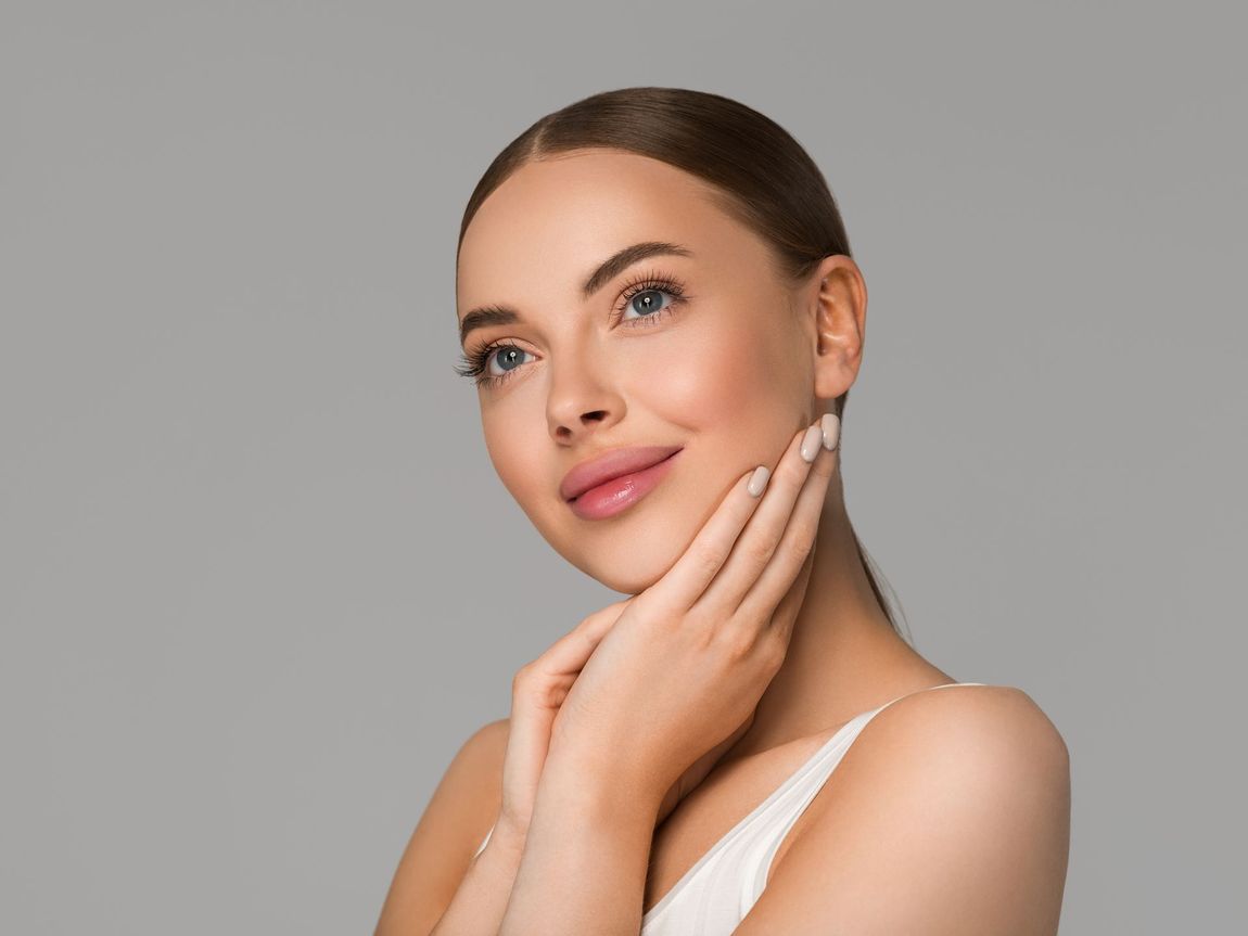 A woman is touching her face with her hands and smiling.