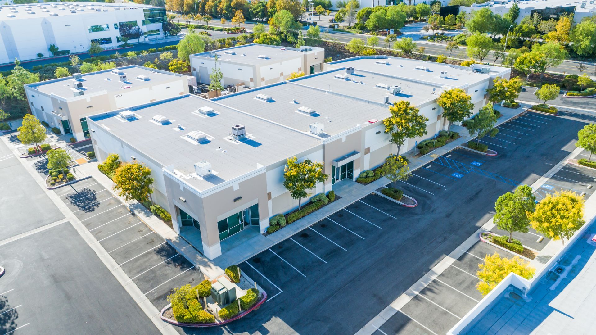 Aerial view of commercial buildings with large parking areas and trees.