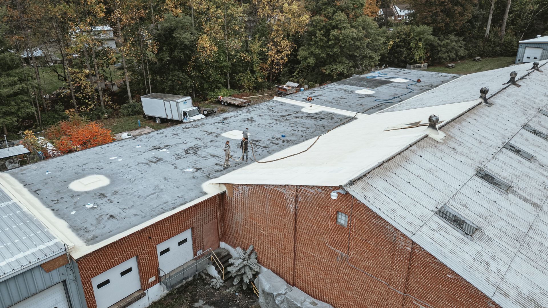 Aerial view of a gray industrial building with a flat roof. A person stands on the roof near a second building.