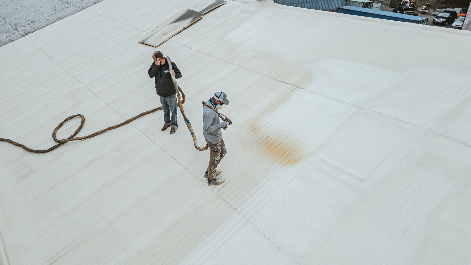 Two people on a white rooftop, holding a hose. One is spraying a brown substance.
