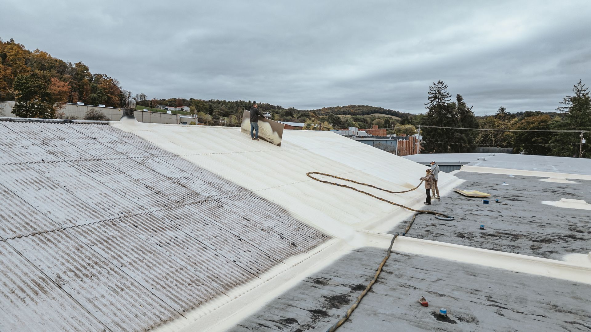 Roofers installing white material on a flat roof under an overcast sky.