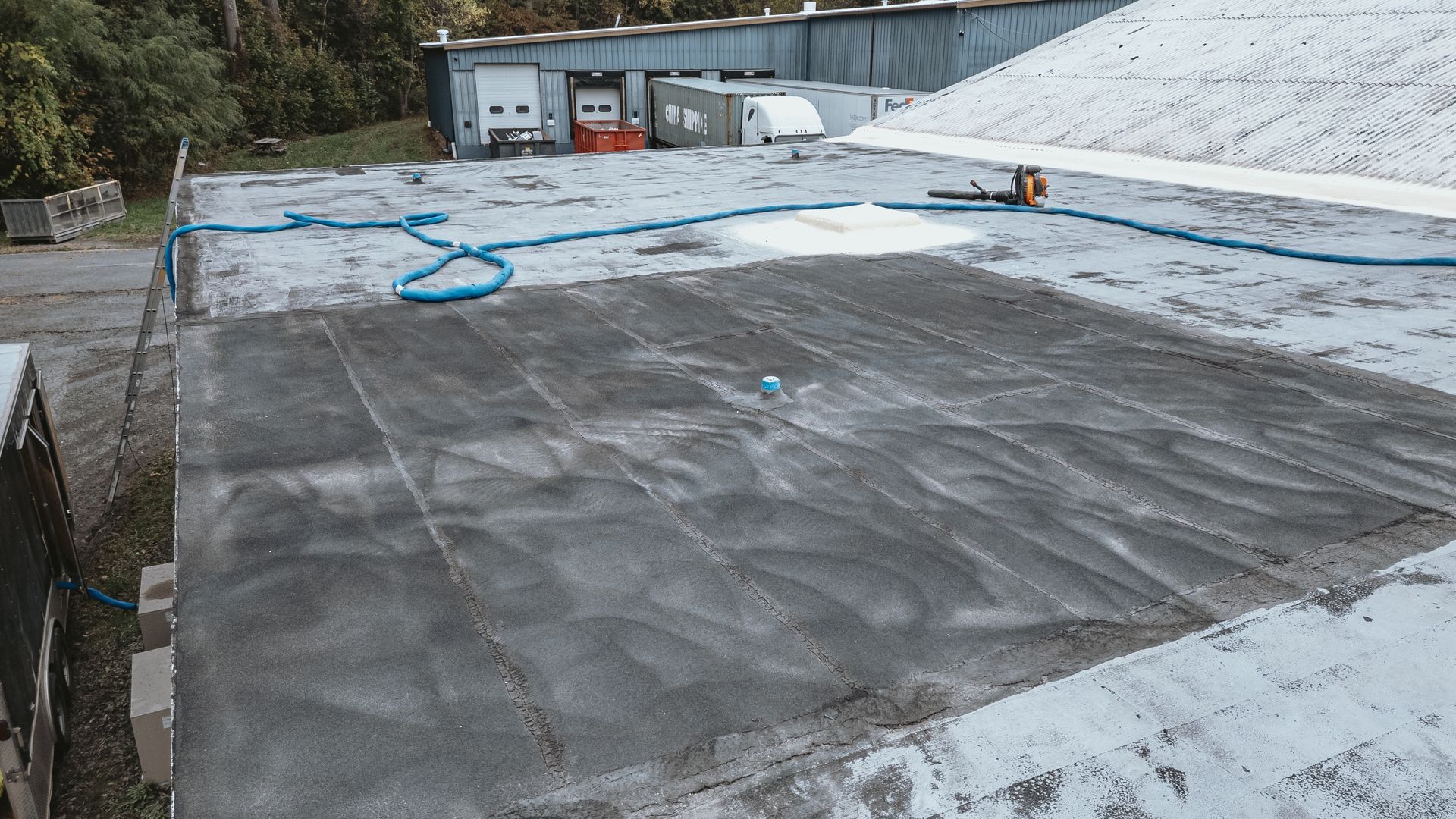 Aerial view of a flat rooftop with blue water lines. Patches of gray and white surfaces.