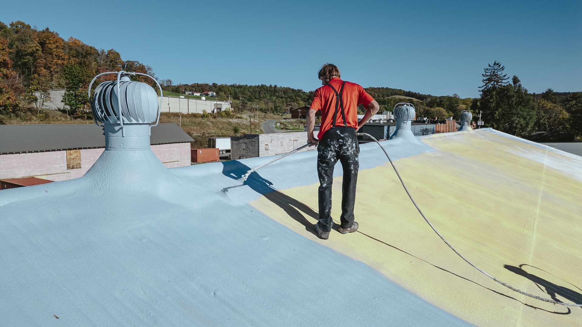 Person in safety harness on a painted roof, blue and yellow sections.