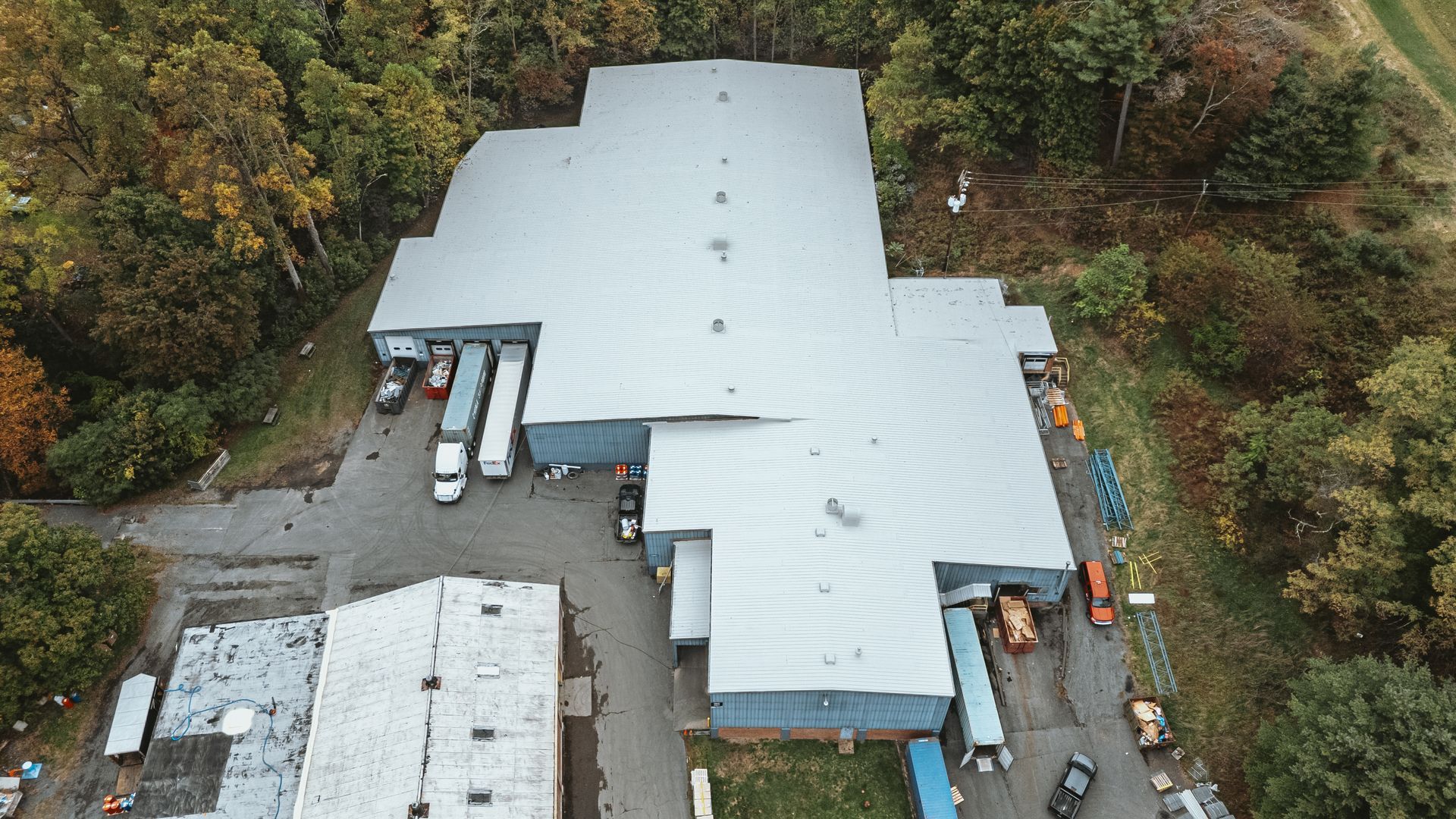 Aerial view of a large warehouse with several trucks and surrounding trees, in a wooded area.