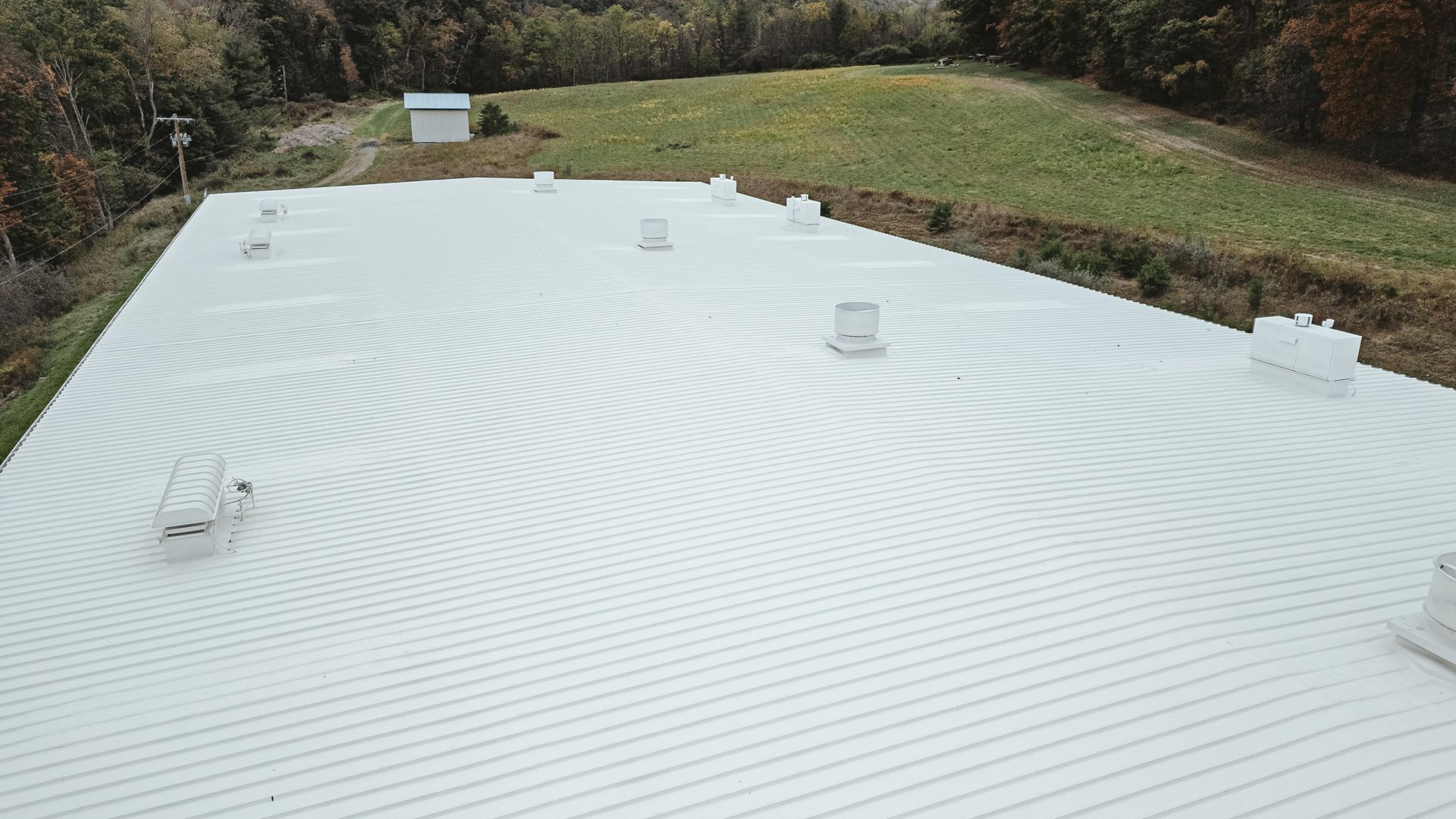White rooftop with a repeating circular pattern, several vents, and a small building in the background.