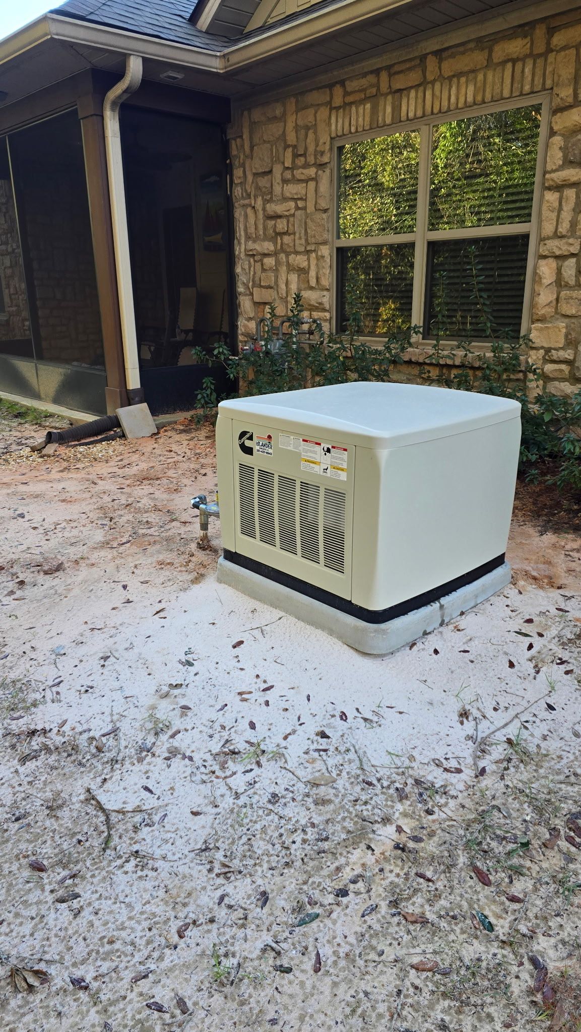A white box is sitting in the dirt in front of a brick house.