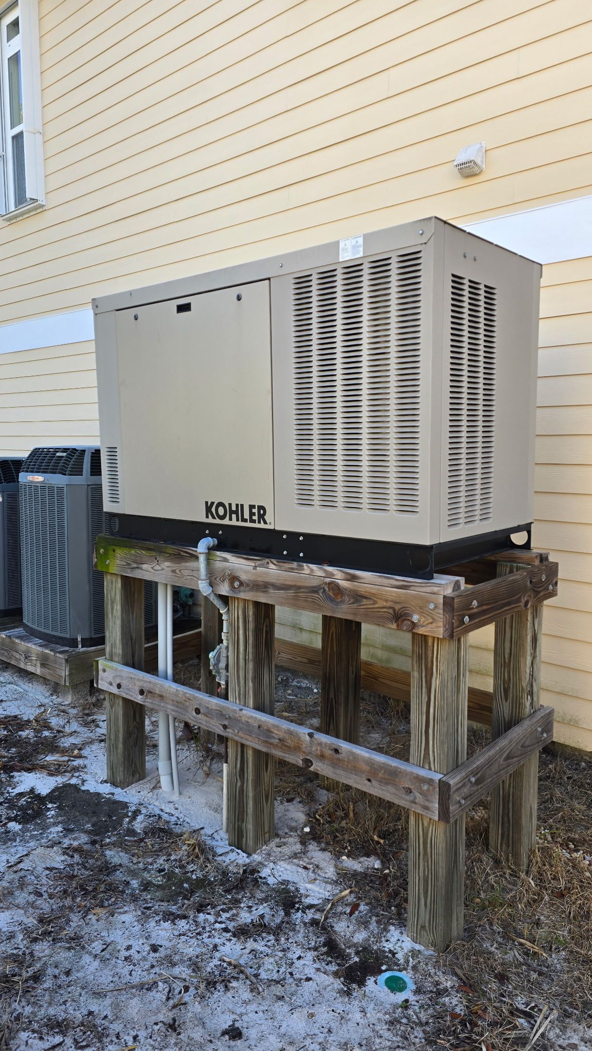 A generator is sitting on a wooden stand outside of a building.