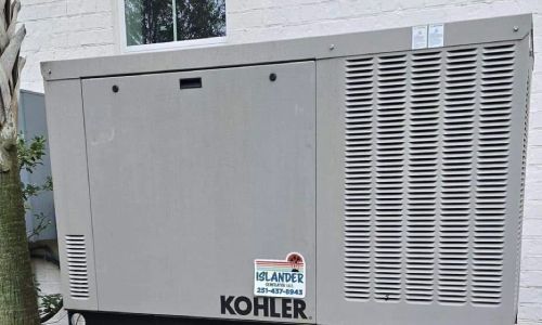 A kohler generator is sitting outside of a house next to a tree.