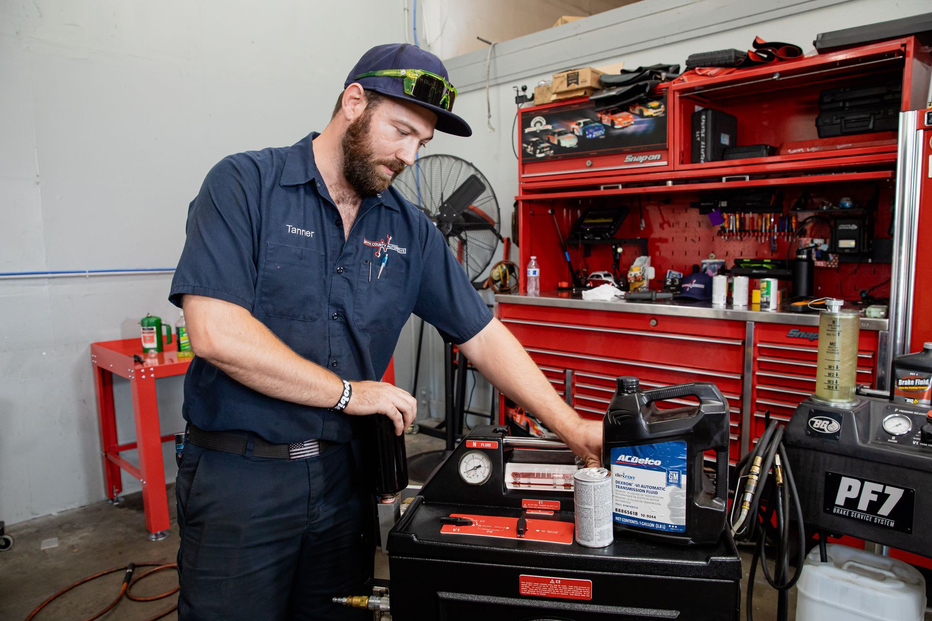Mechanic in a blue uniform working on a machine, inside a garage with tools and a cabinet.