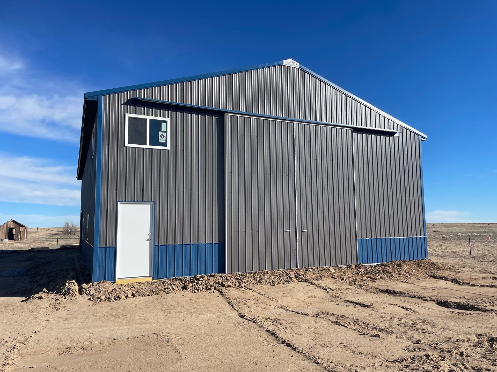 Small corrugated metal shed in a barren field under a clear blue sky