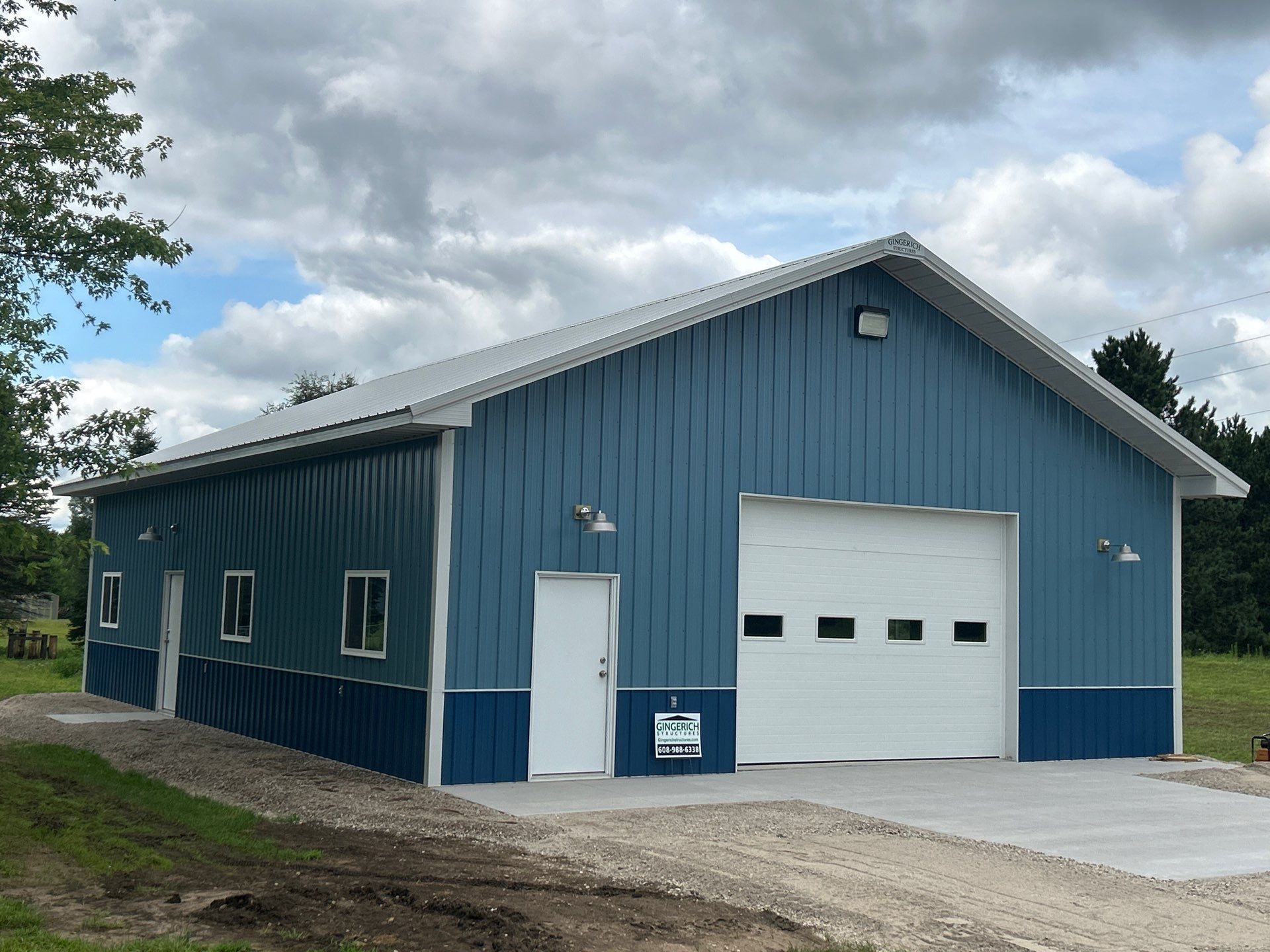 Red barn with white trim against a blue sky, with a driveway and trees.