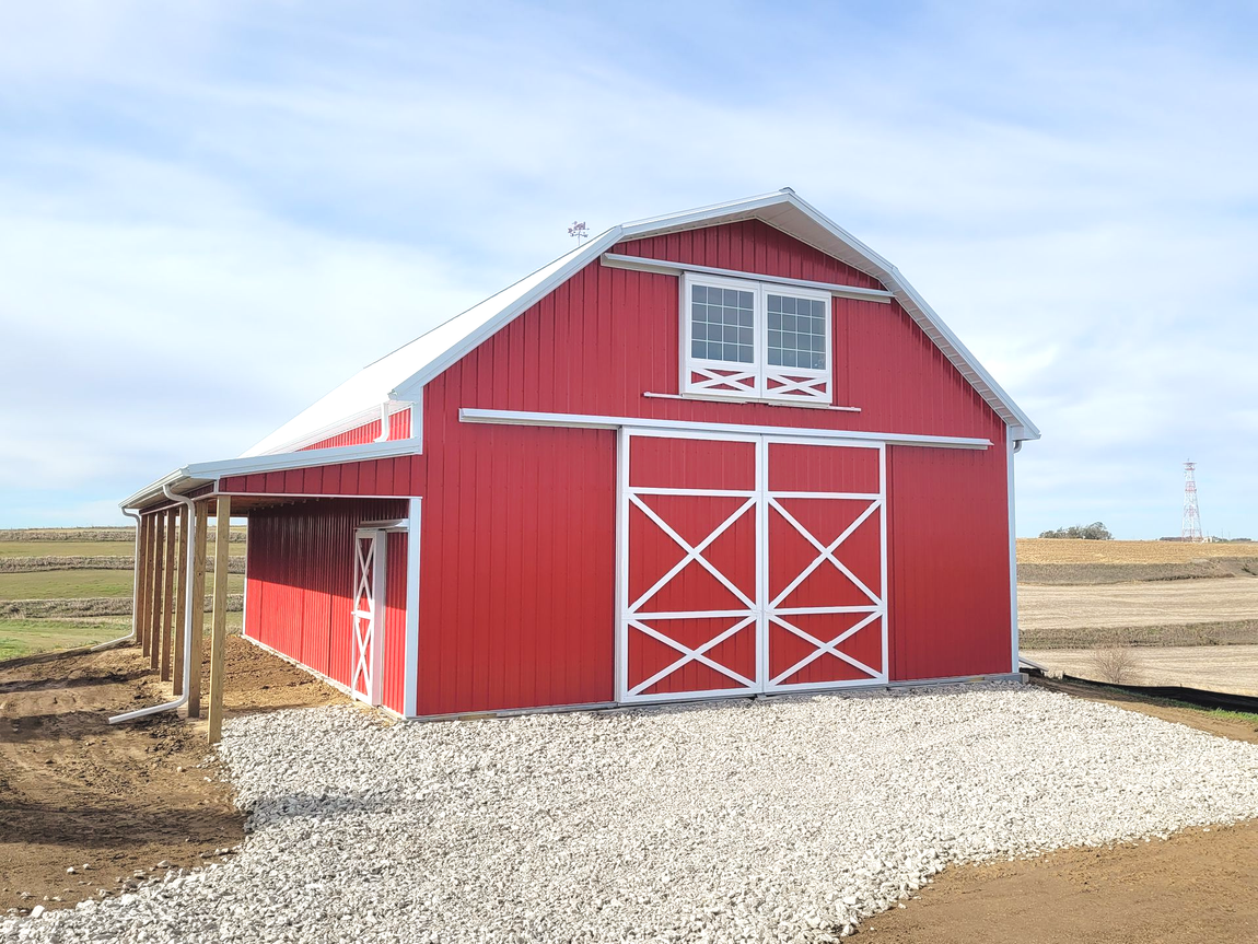 Red barn with white trim and sliding doors, gravel path, and blue sky.