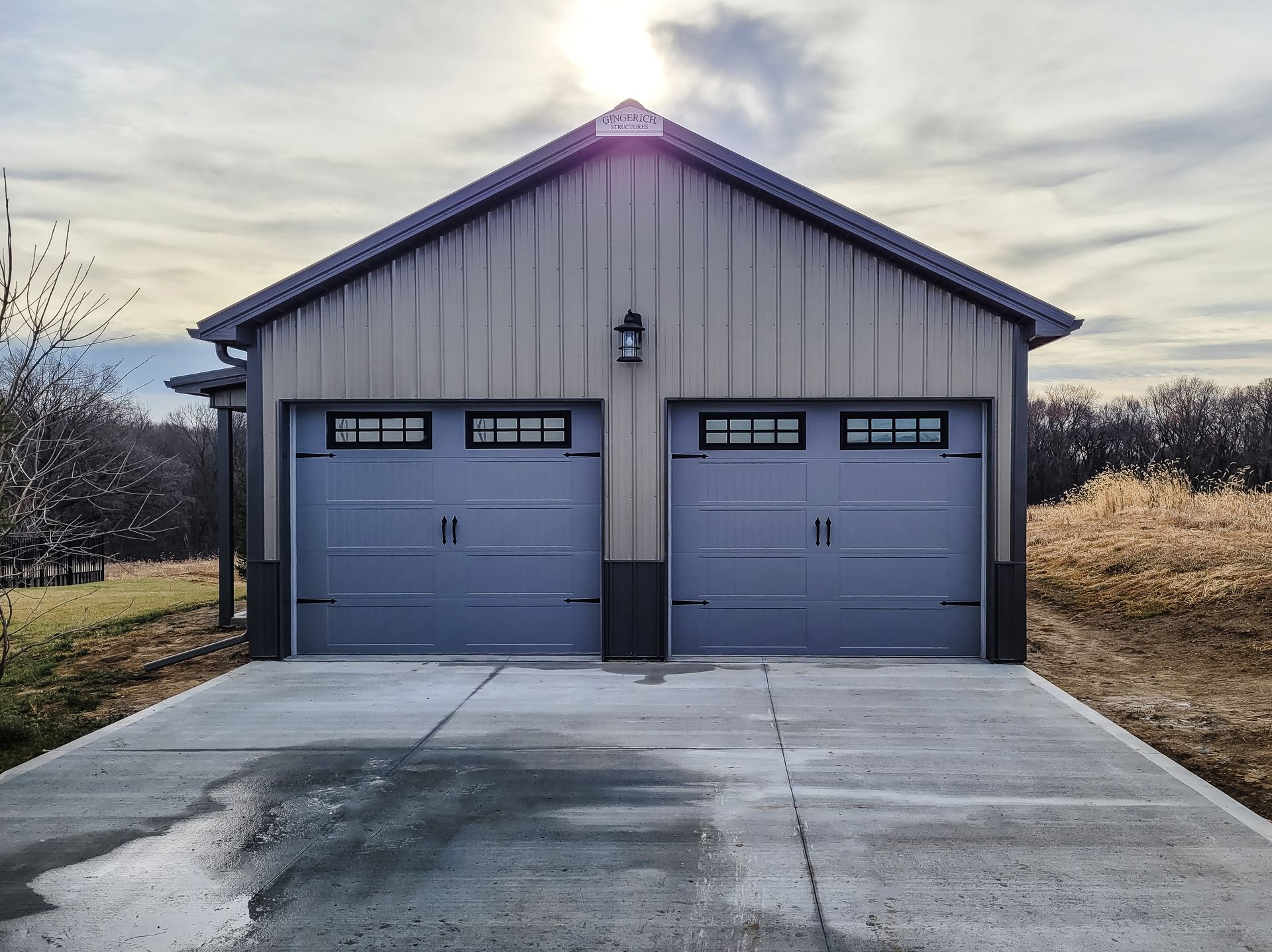 Large metal agricultural building with silos in the background under a blue sky.