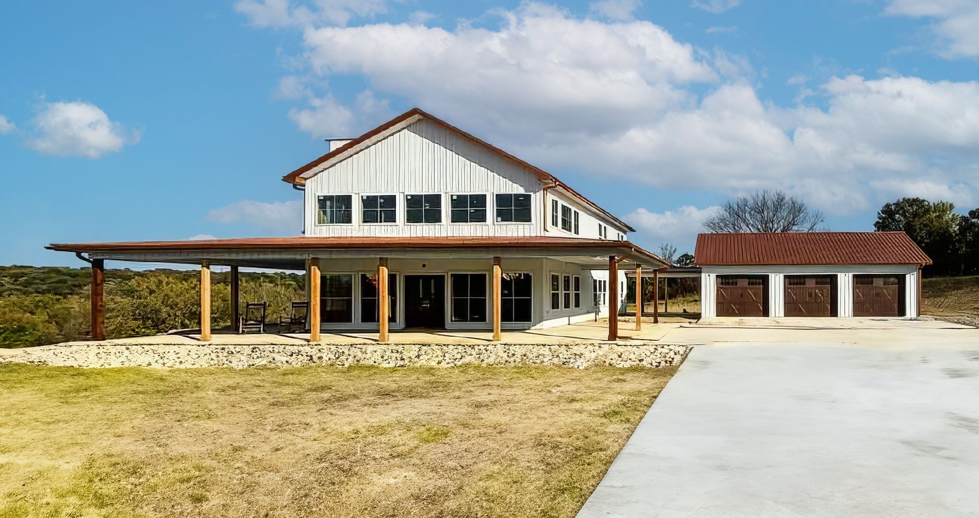 White farmhouse with covered porch, two-story, and attached garage on a sunny day.