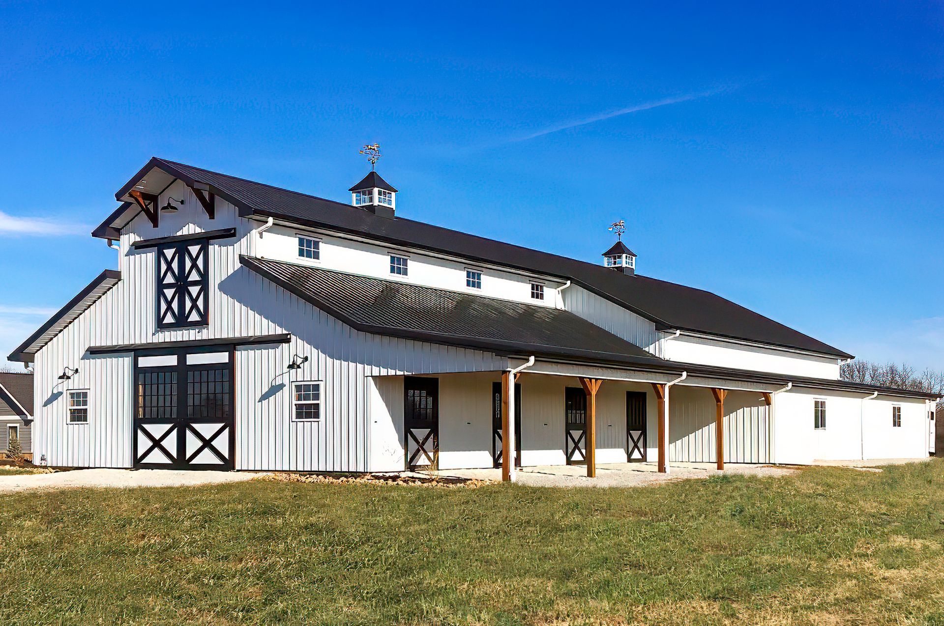 White and black barn with a dark roof under a clear, blue sky.