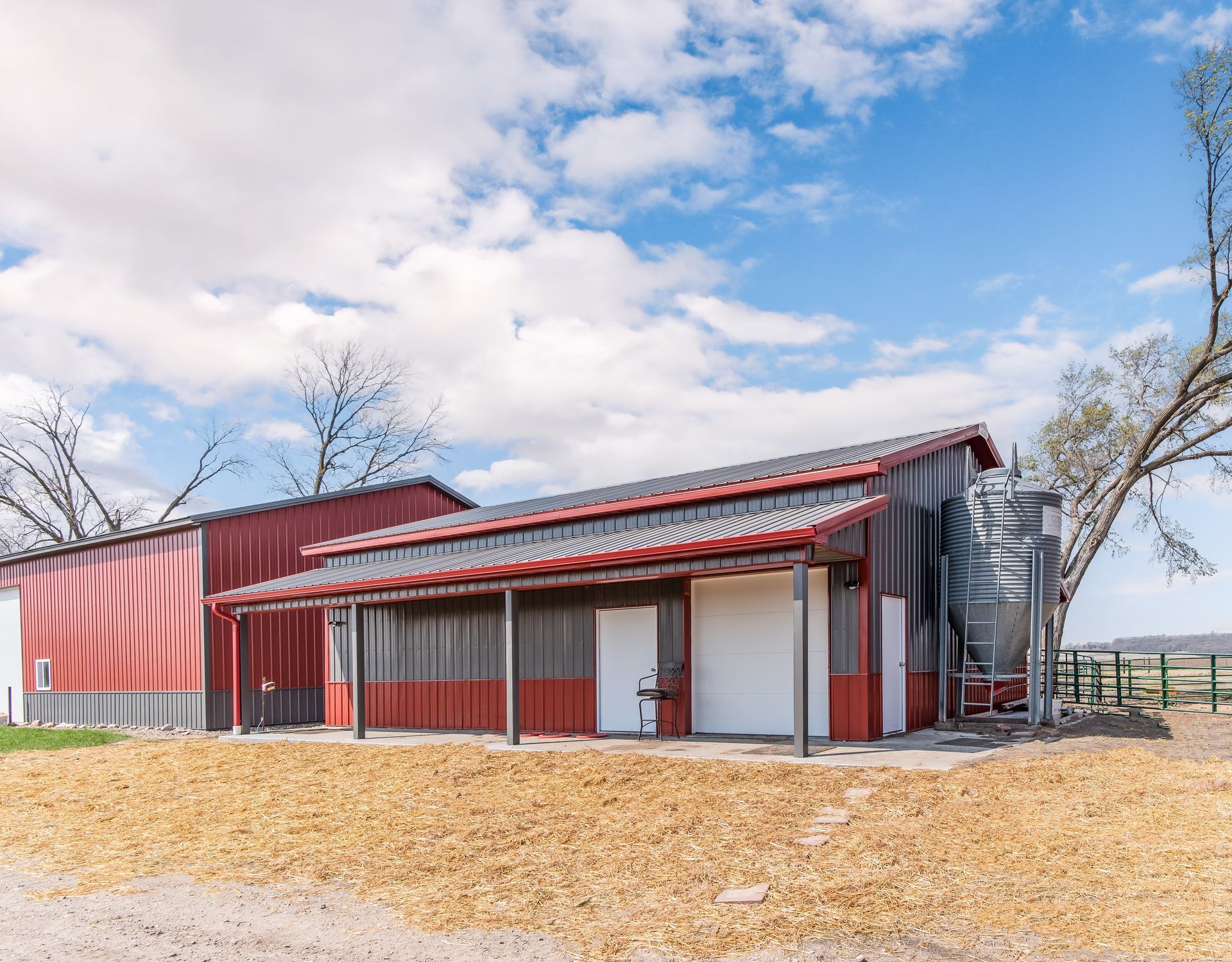A light gray and black metal building with a stone base, a brown wooden porch, and a black roof.