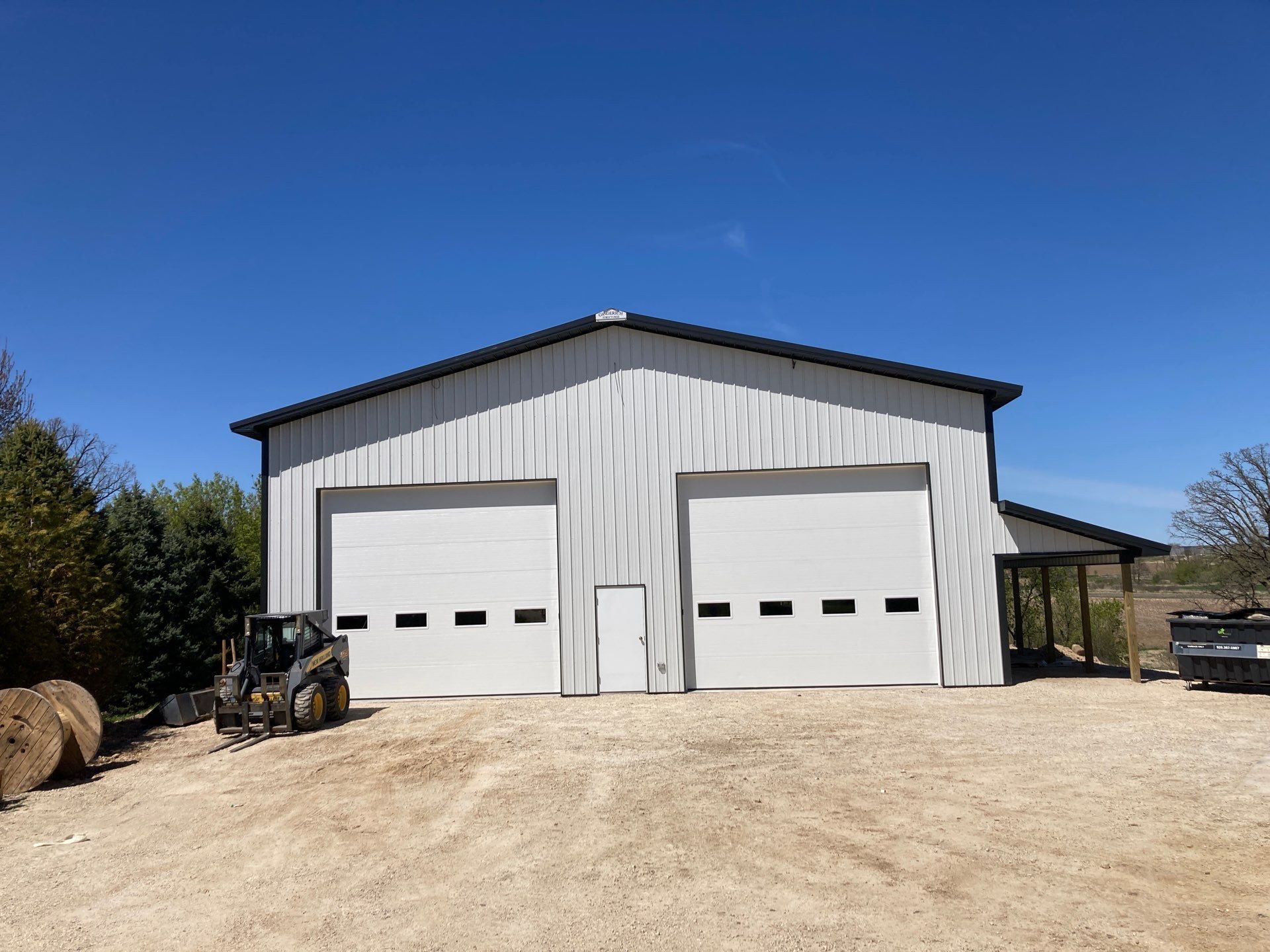 Large metal agricultural building with silos in the background under a blue sky.