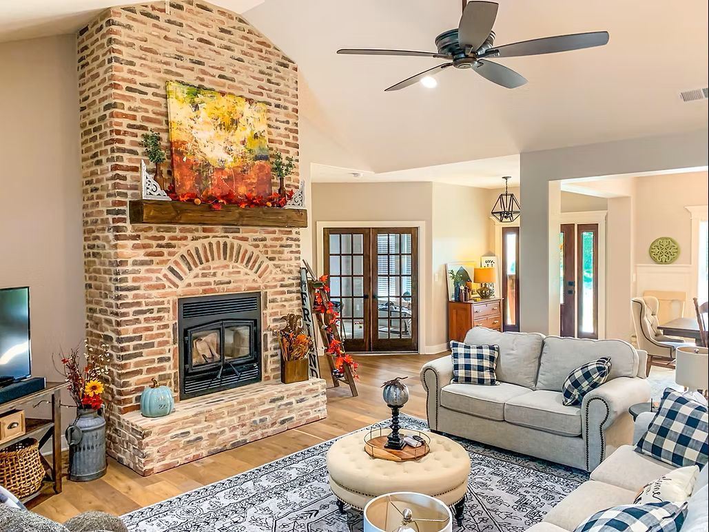A gray house with a screened-in porch on a grassy field under a cloudy sky.