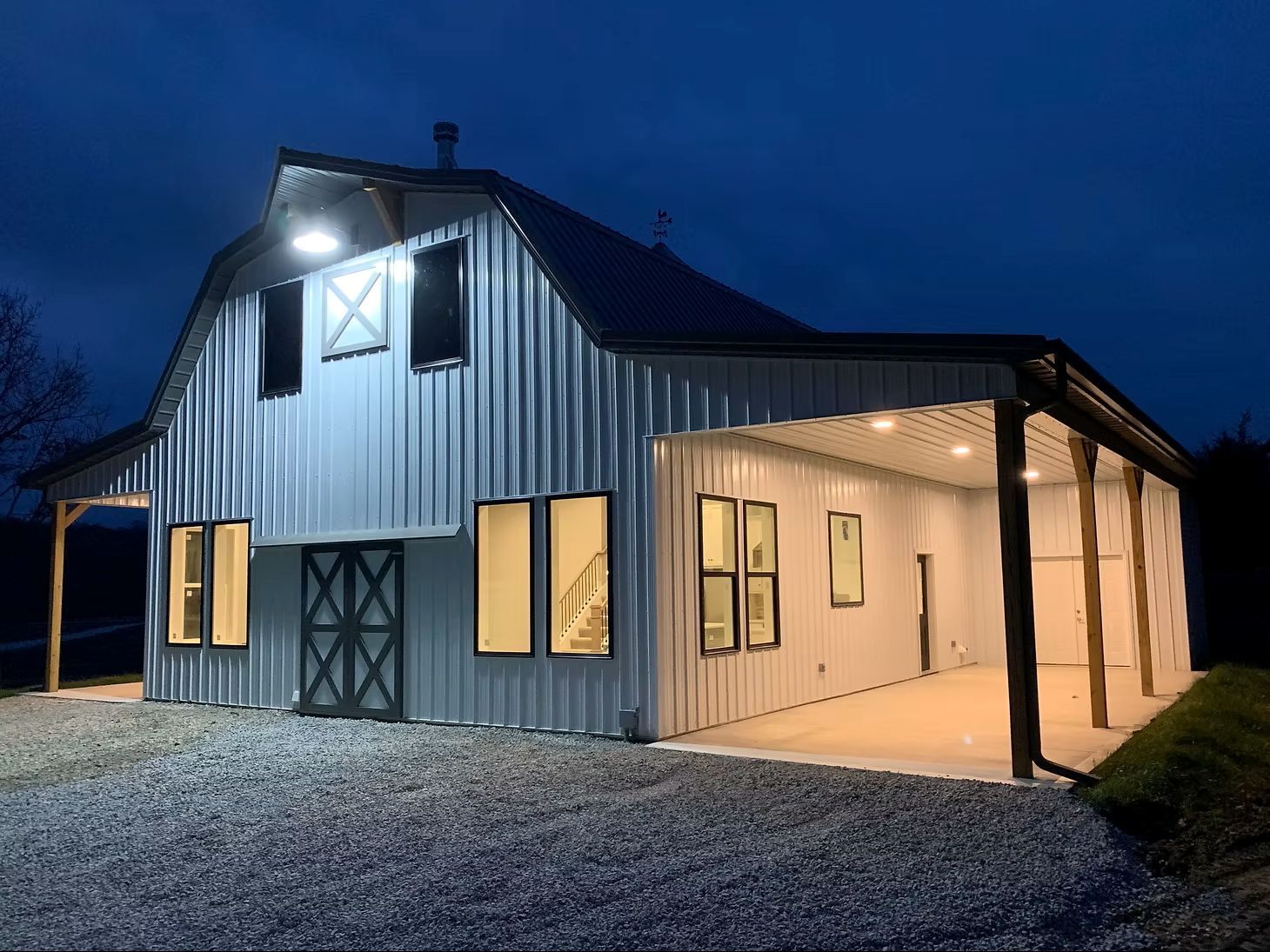 Night picture of Post Frame building with two lean to's on the sides and a white barn looking exterior.
