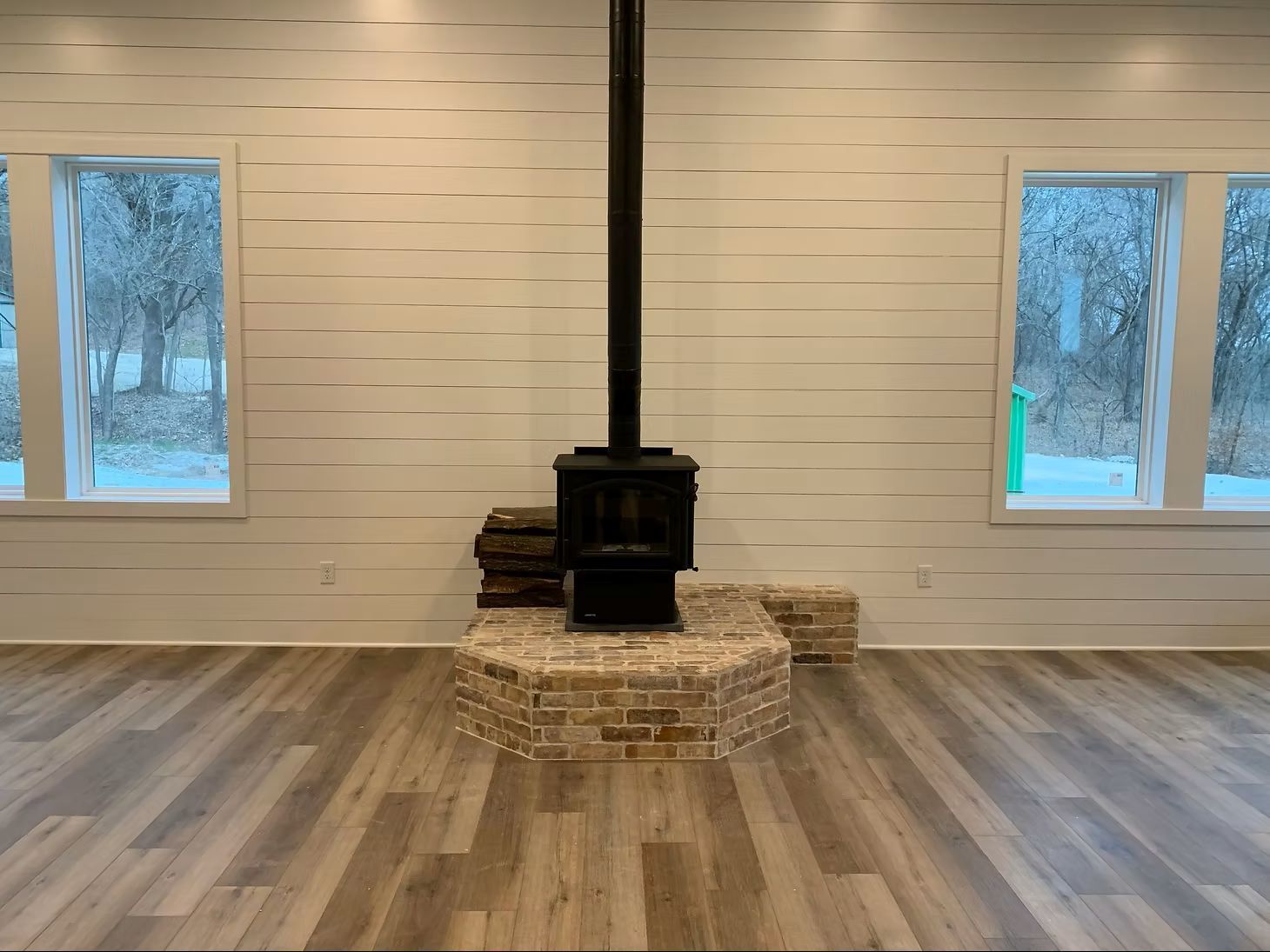 Old wood fireplace free standing against a white wall with windows on either side. 