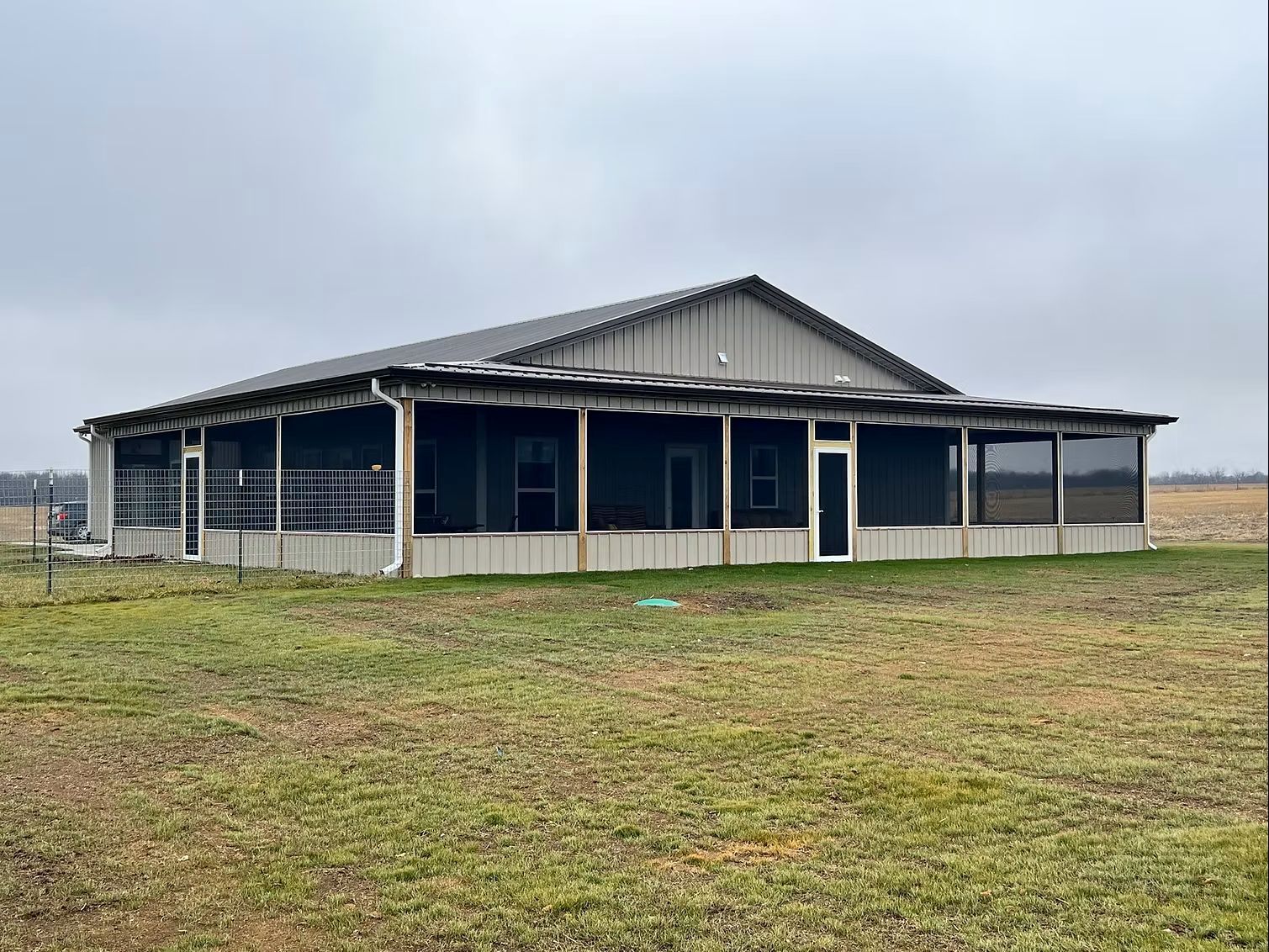 Large grey building with wrap around porch. Single floor in open land. 