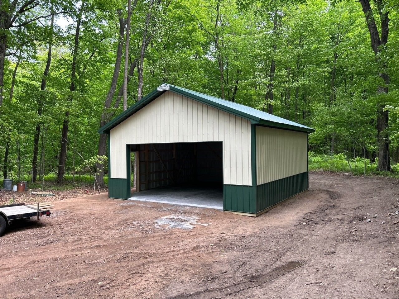 A large, new metal barn with white and dark brown siding, a covered porch, and a concrete slab.