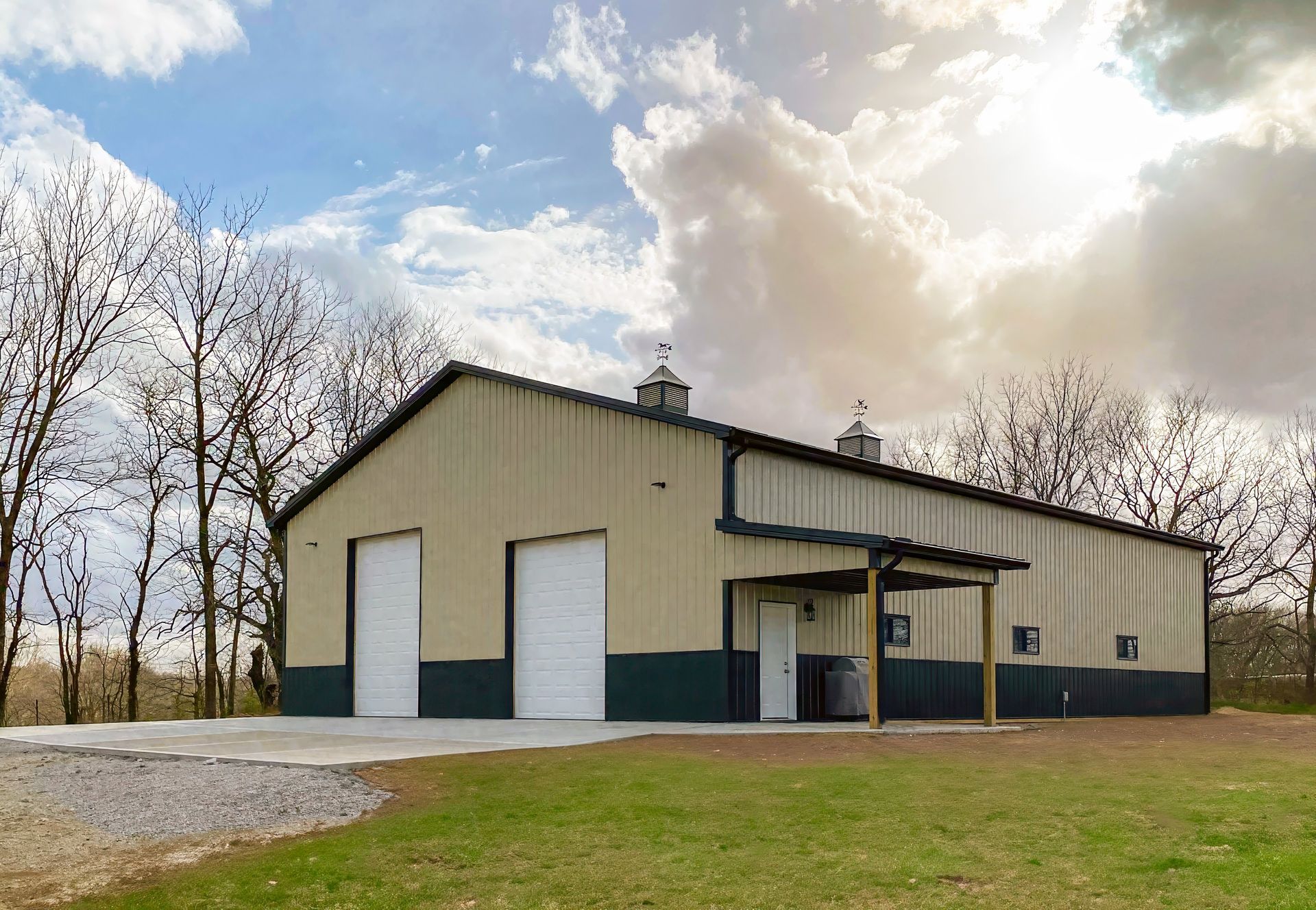 Tan and green metal barn with two garage doors and a small covered entryway, under a cloudy sky.