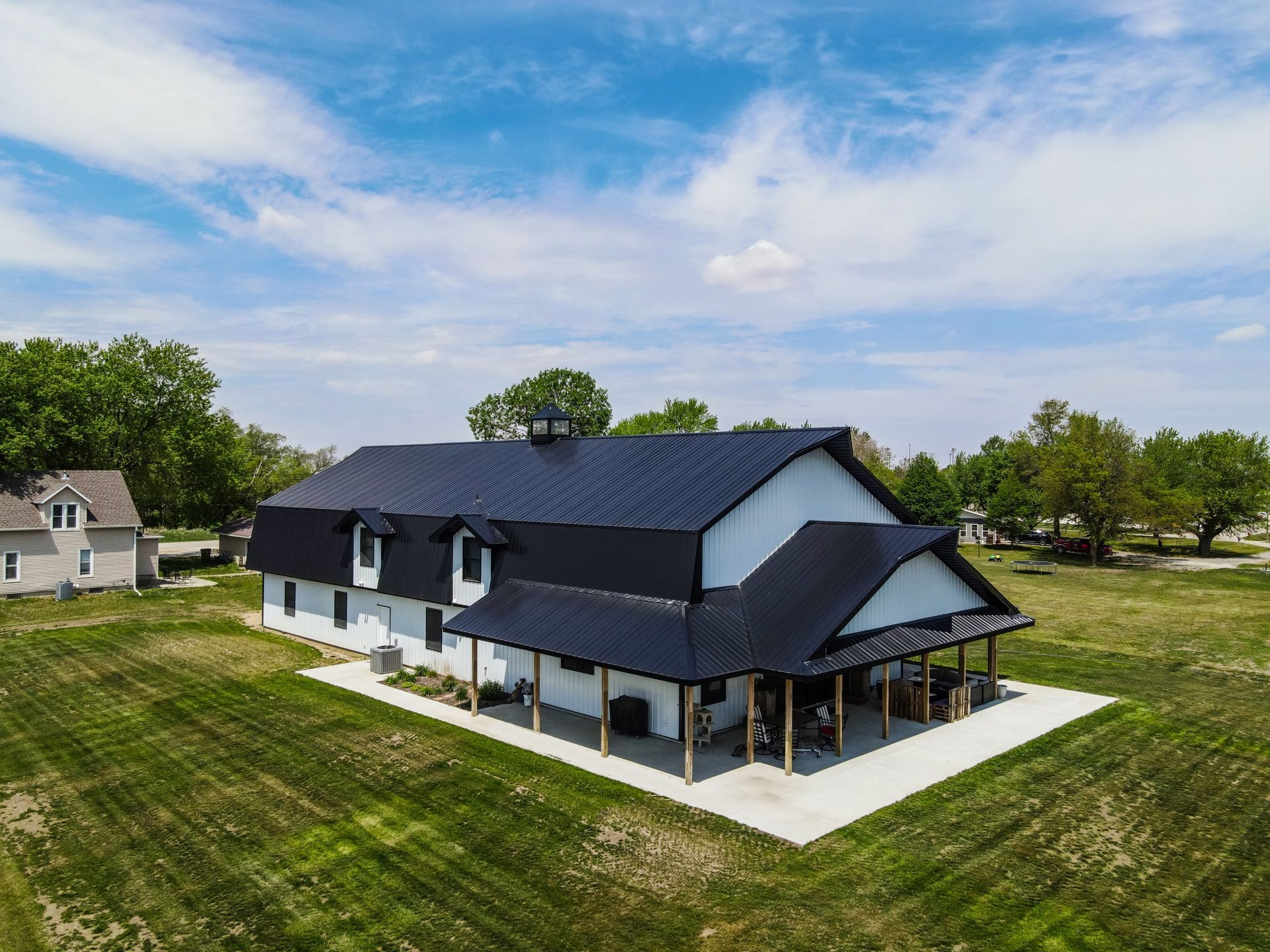 White and black barn-style building with a porch on a green field under a blue sky.