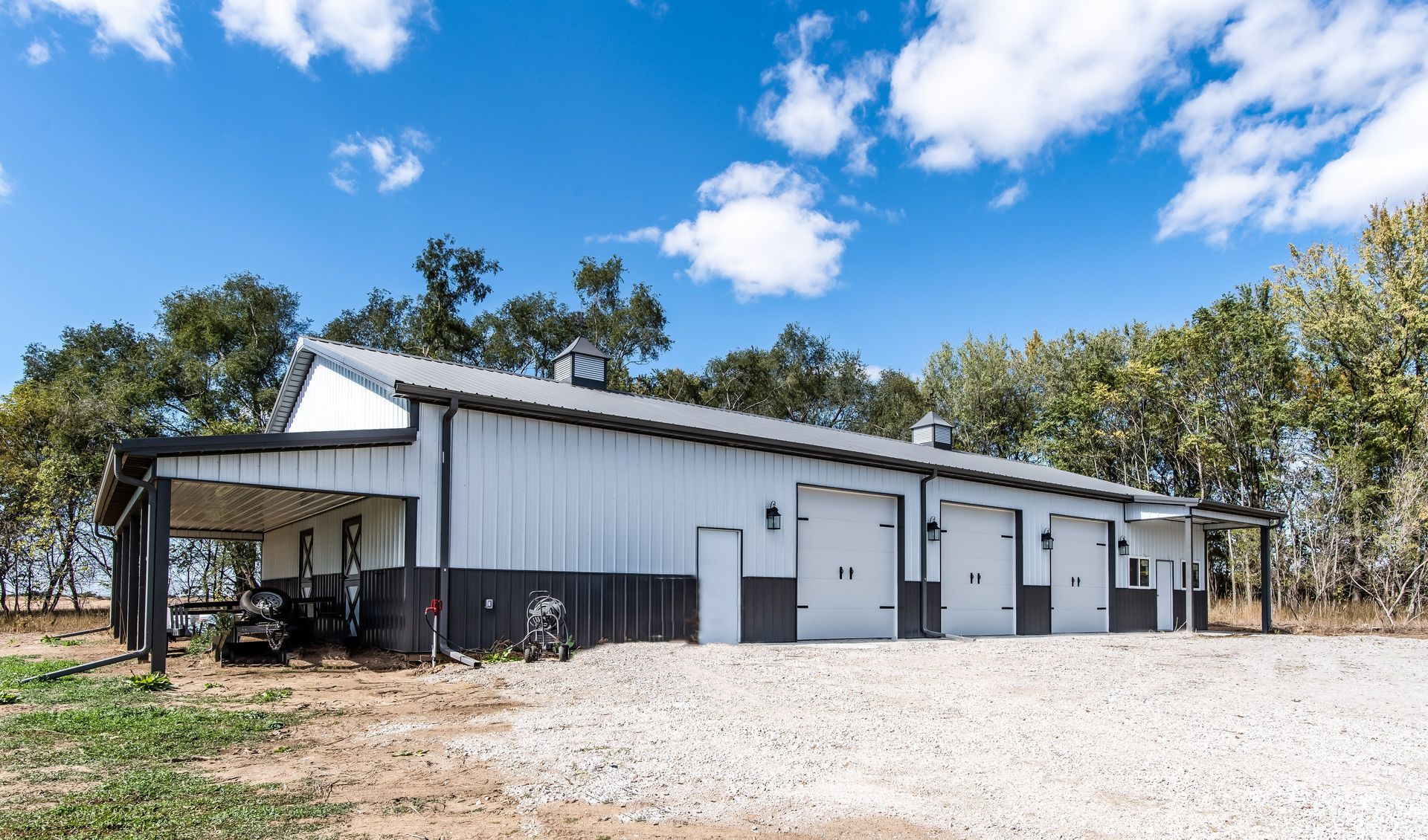 White and black metal building with three garage doors under a blue sky.