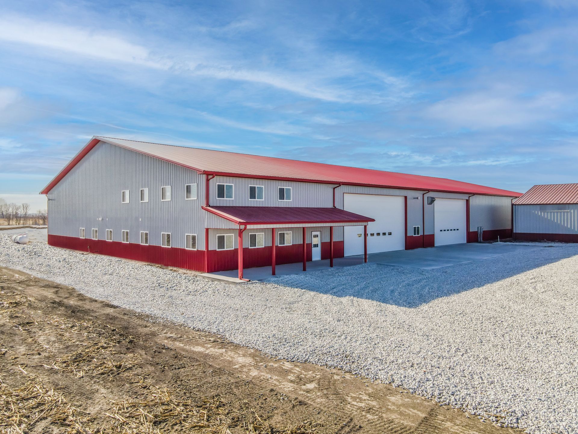 Large red and gray metal building with a gravel driveway under a blue sky.