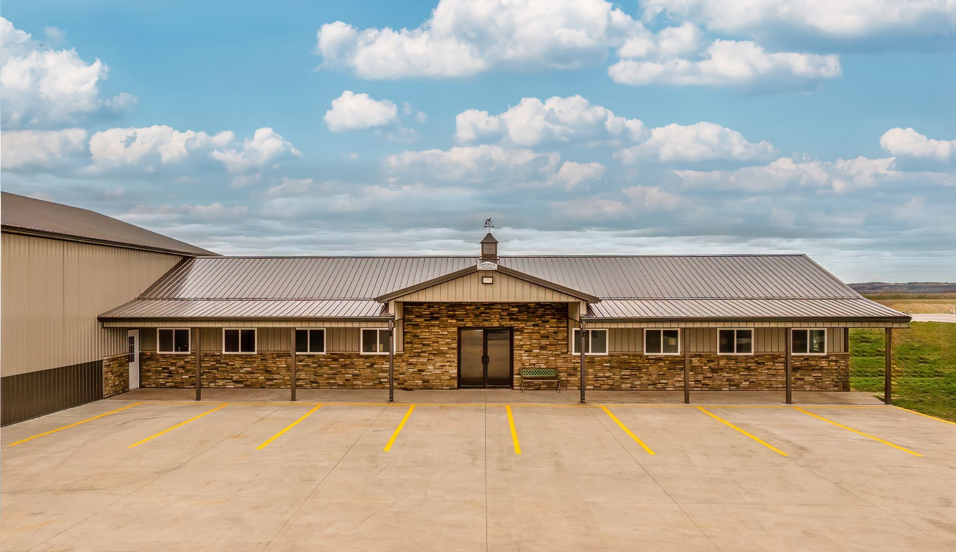 Stone building with metal roof and parking lot under blue sky.