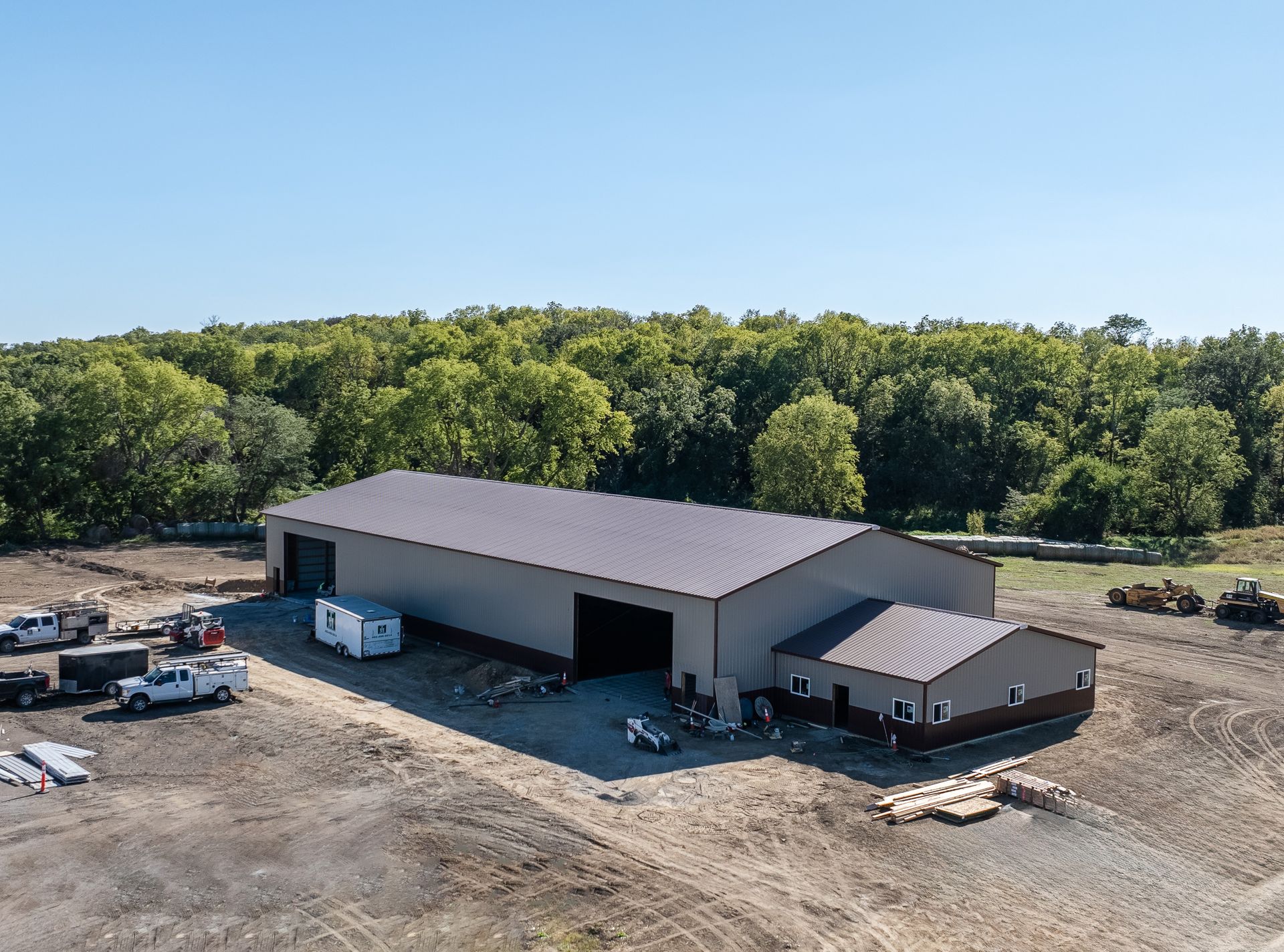Large gray industrial building with a smaller attached building; construction materials and vehicles nearby.