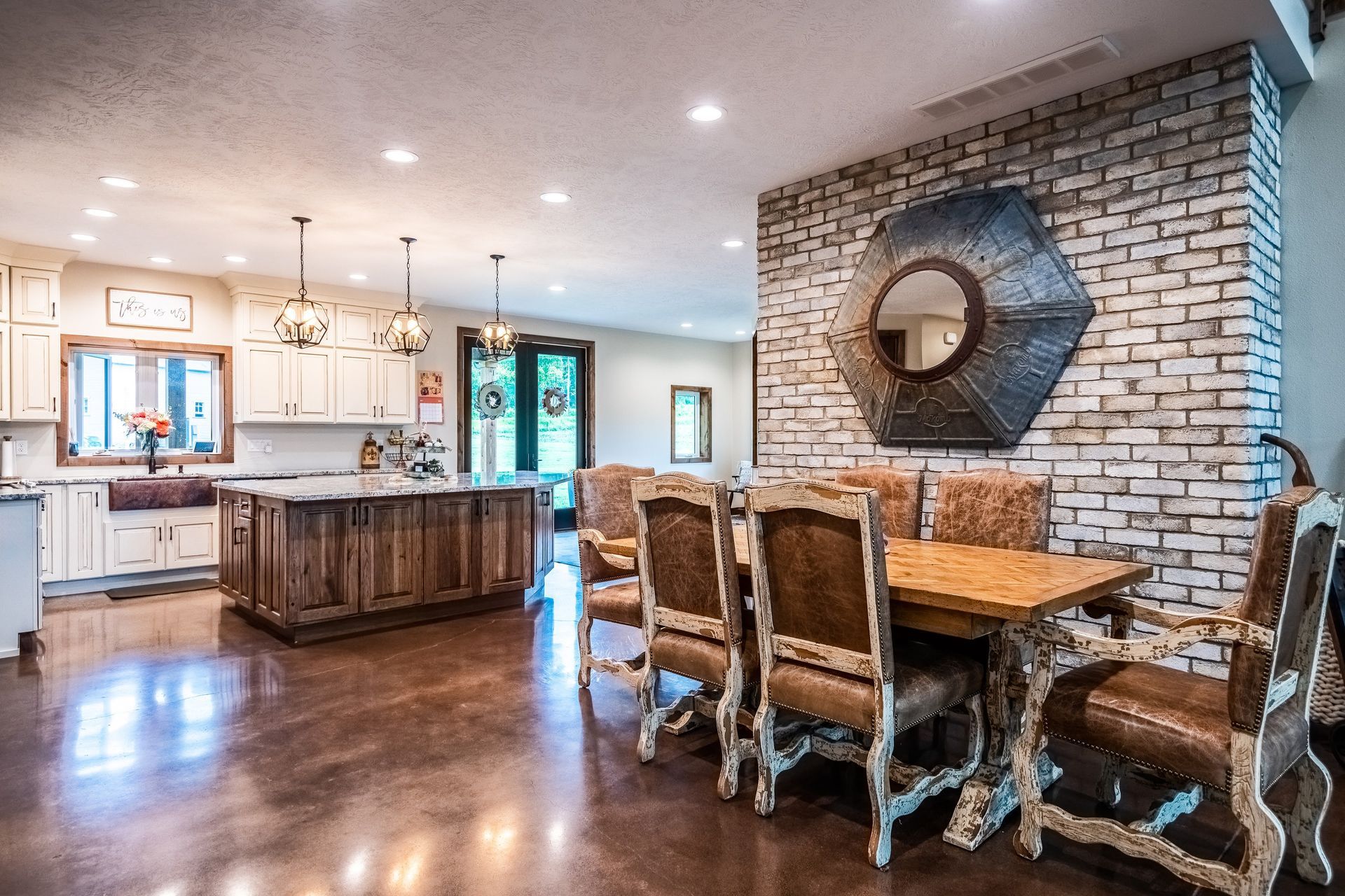 Spacious open kitchen and dining area with wood floors, exposed brick wall, and ornate wooden table and chairs.