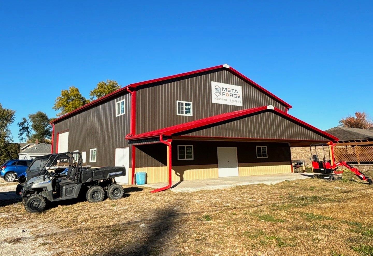 Brown metal building with red trim, a covered porch, and a six-wheeled vehicle parked in front.