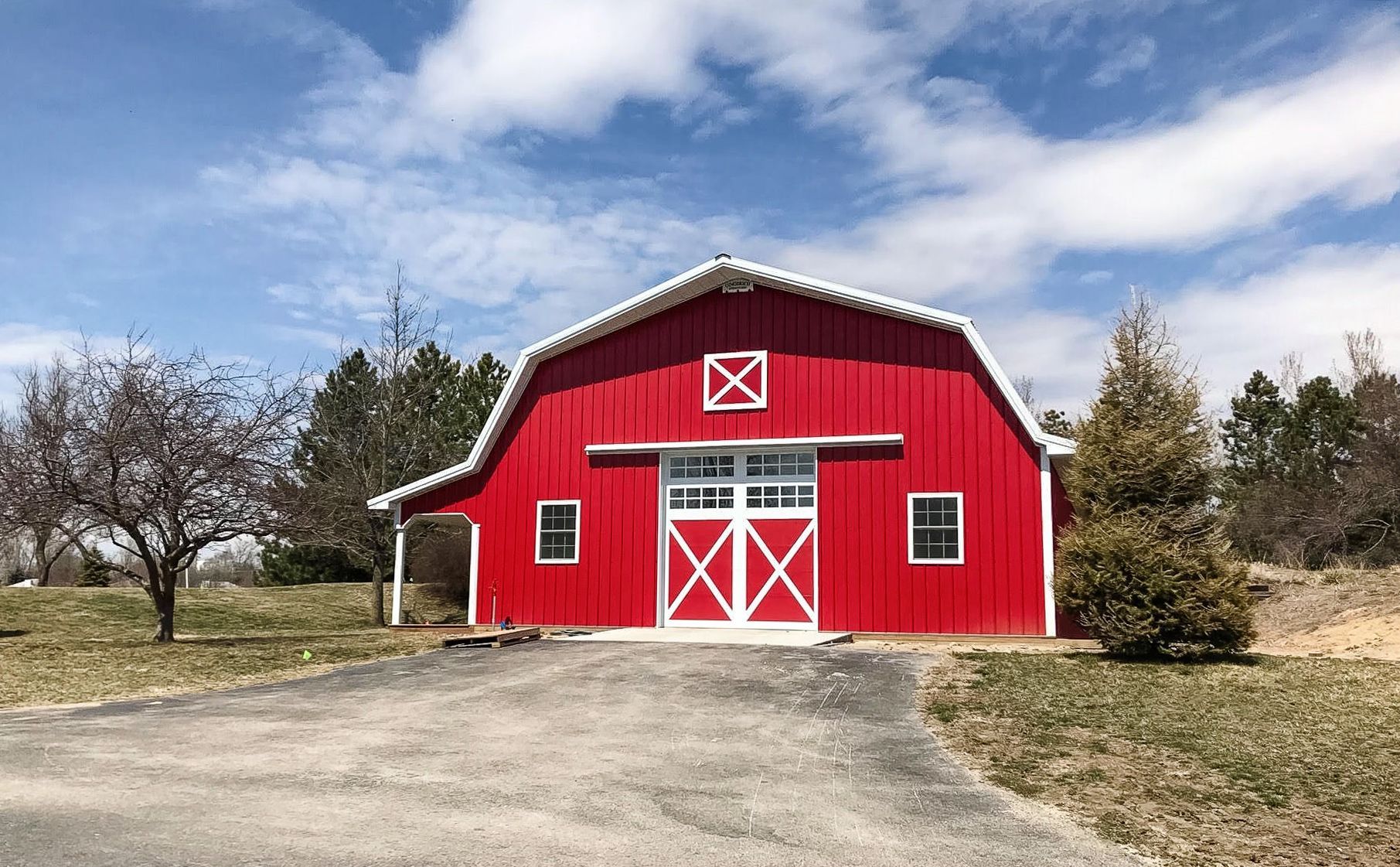 Red barn with white trim, on a sunny day, blue sky, and clouds.