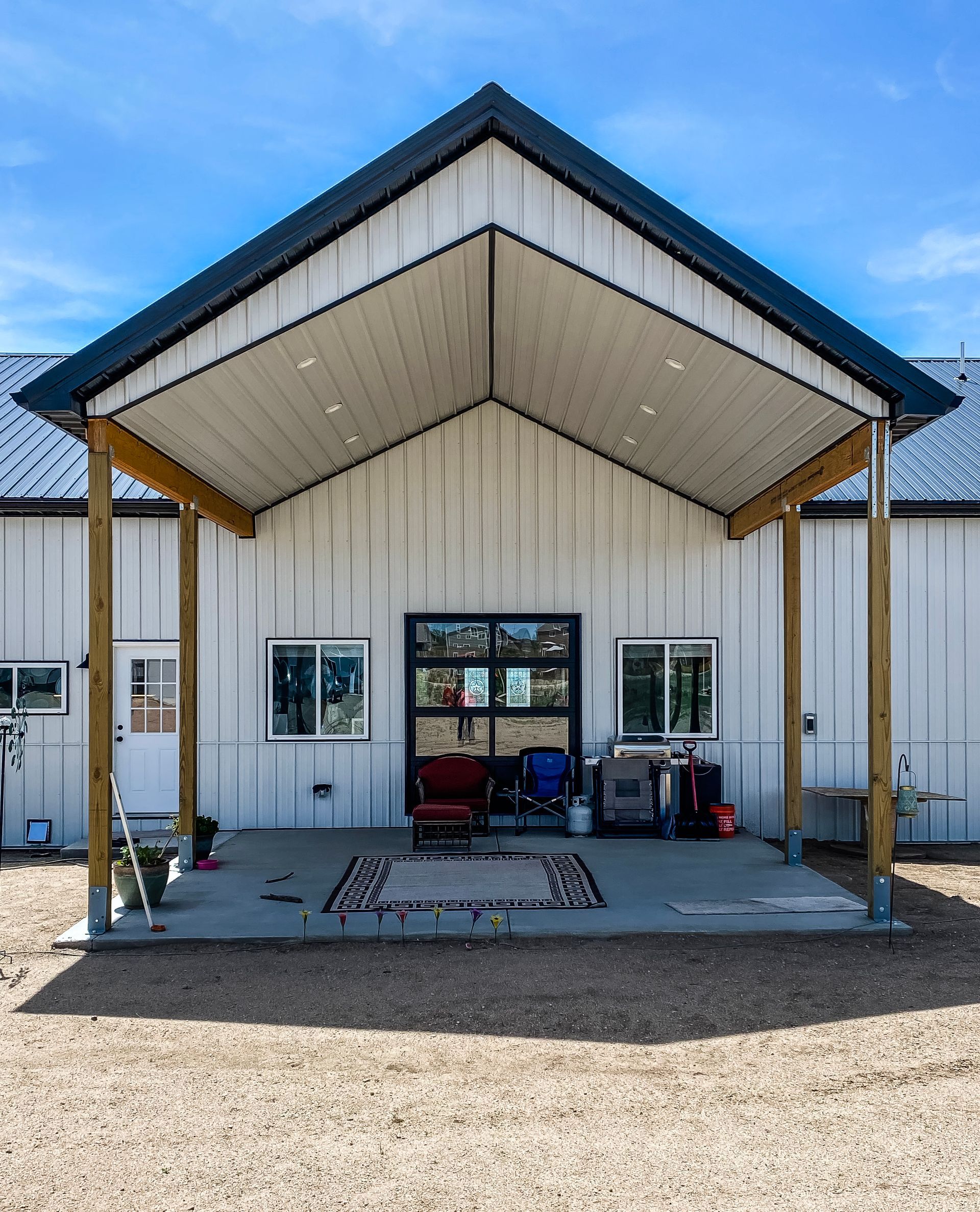 White building with porch, black roof, and glass door. Two wooden beams support the porch.