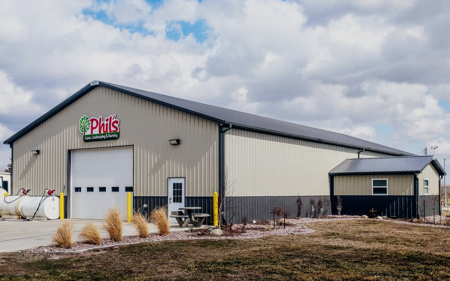 A large metal building, Phil's logo above a white garage door. Small outbuilding to the right.