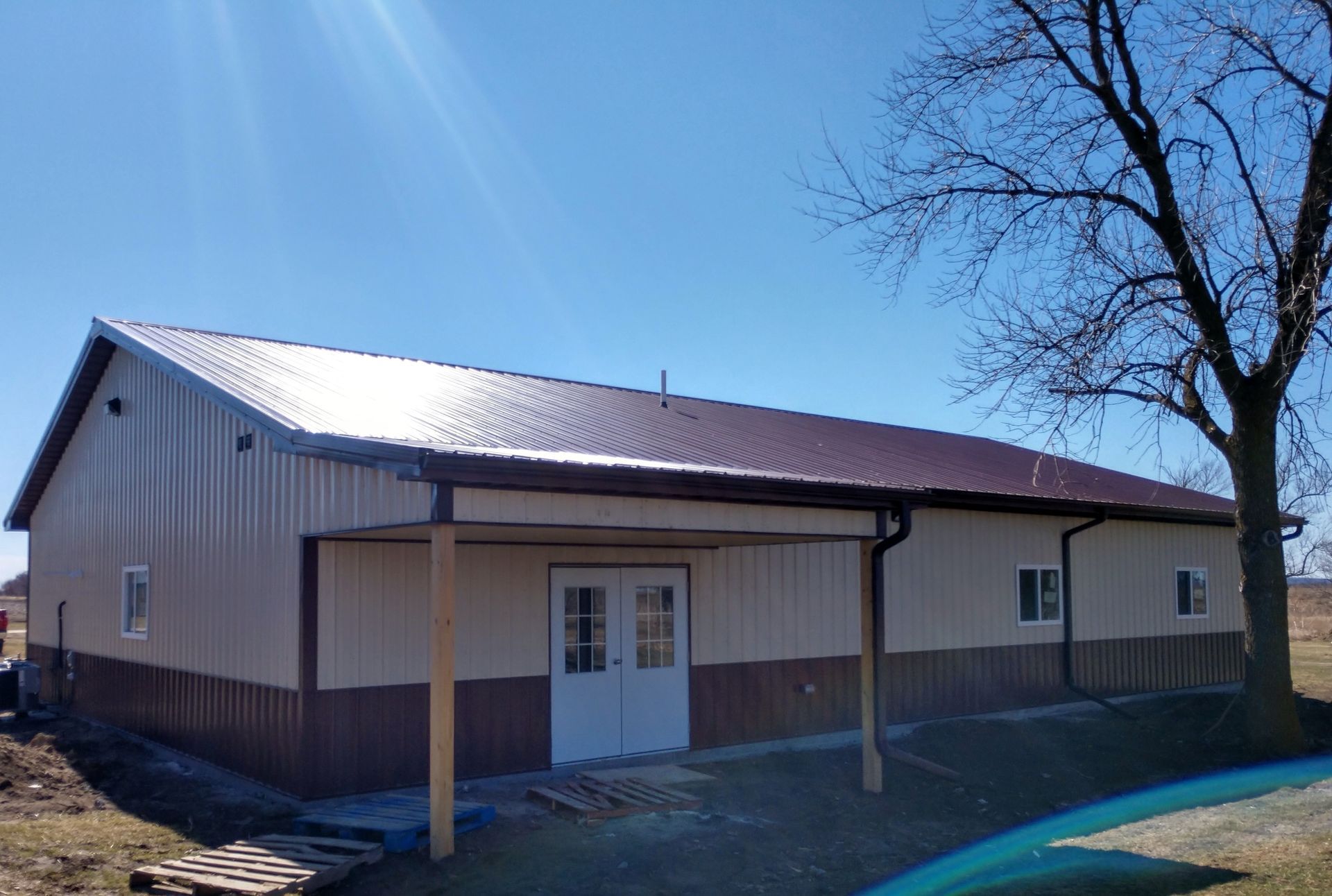 A large metal building with a brown roof, tan walls, and a brown lower wall section on a sunny day.