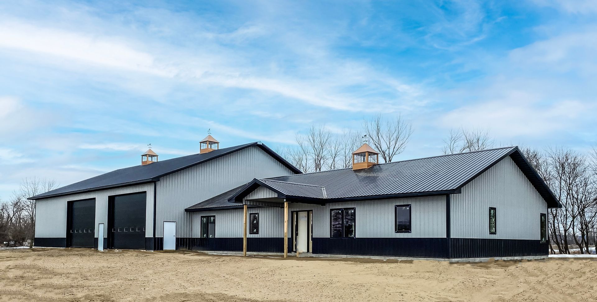 A large gray metal building with black trim and a dark roof, under a blue sky.