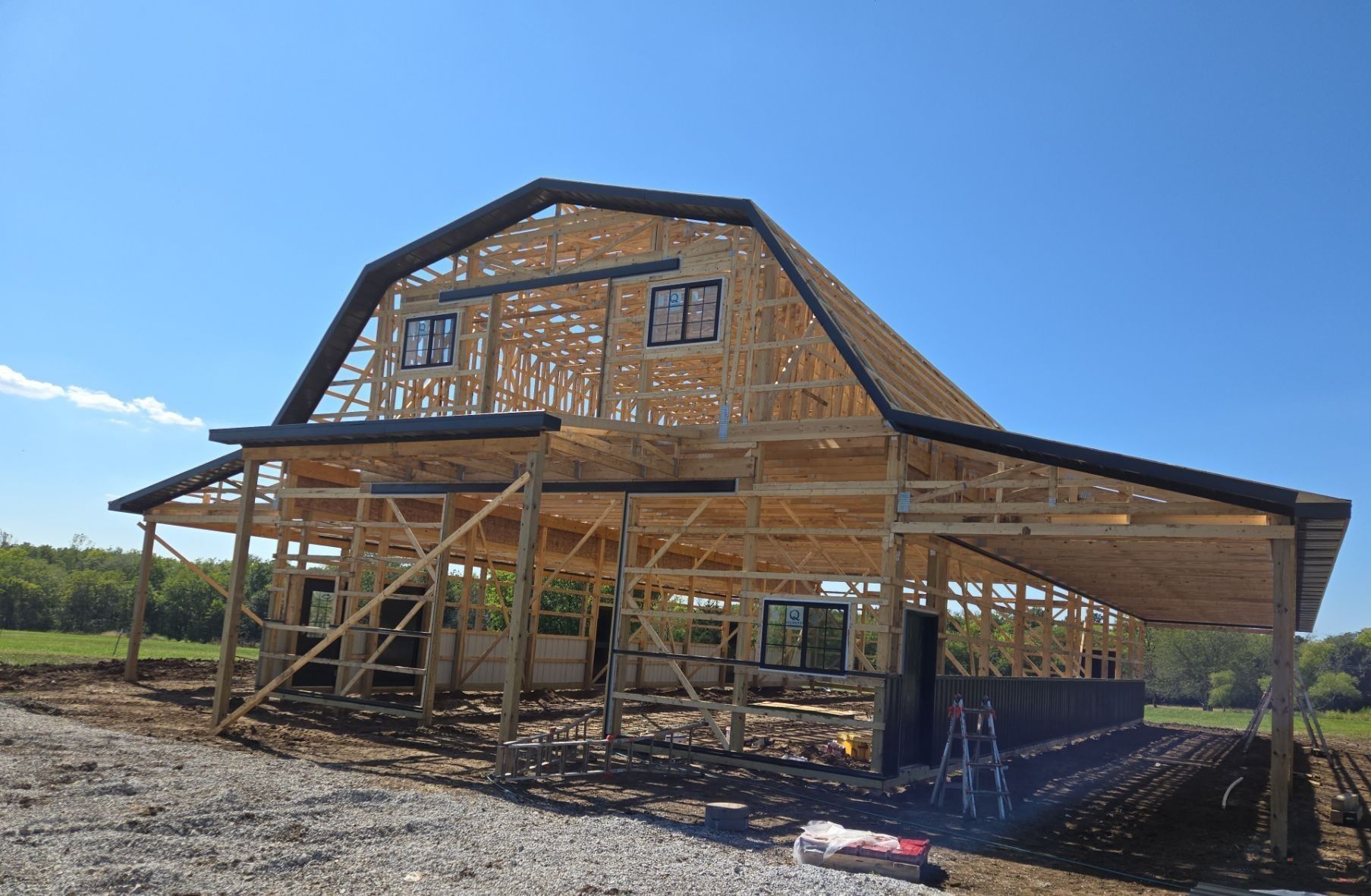 Barn under construction with wooden frame, black roofing, and blue sky.
