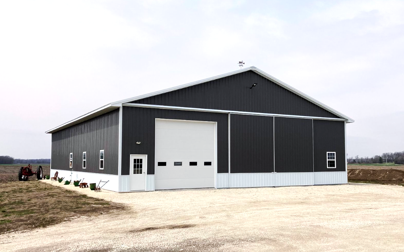 Dark gray metal agricultural building with white trim, large garage door, and small side door.