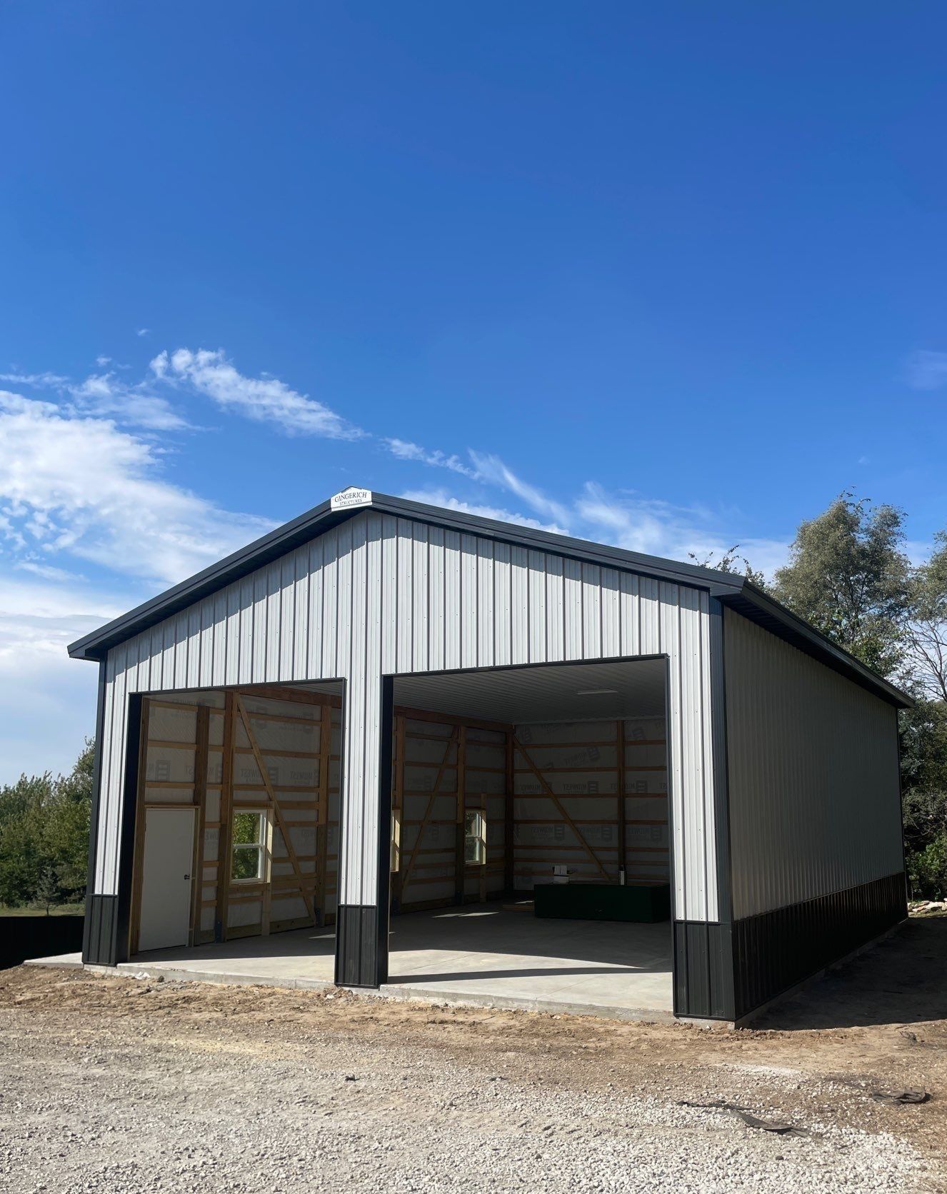 Metal building with two garage door openings, grey walls, black trim, and blue sky.