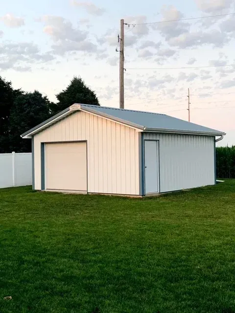 White metal garage with a gray roof on a grassy lawn under a cloudy sky.