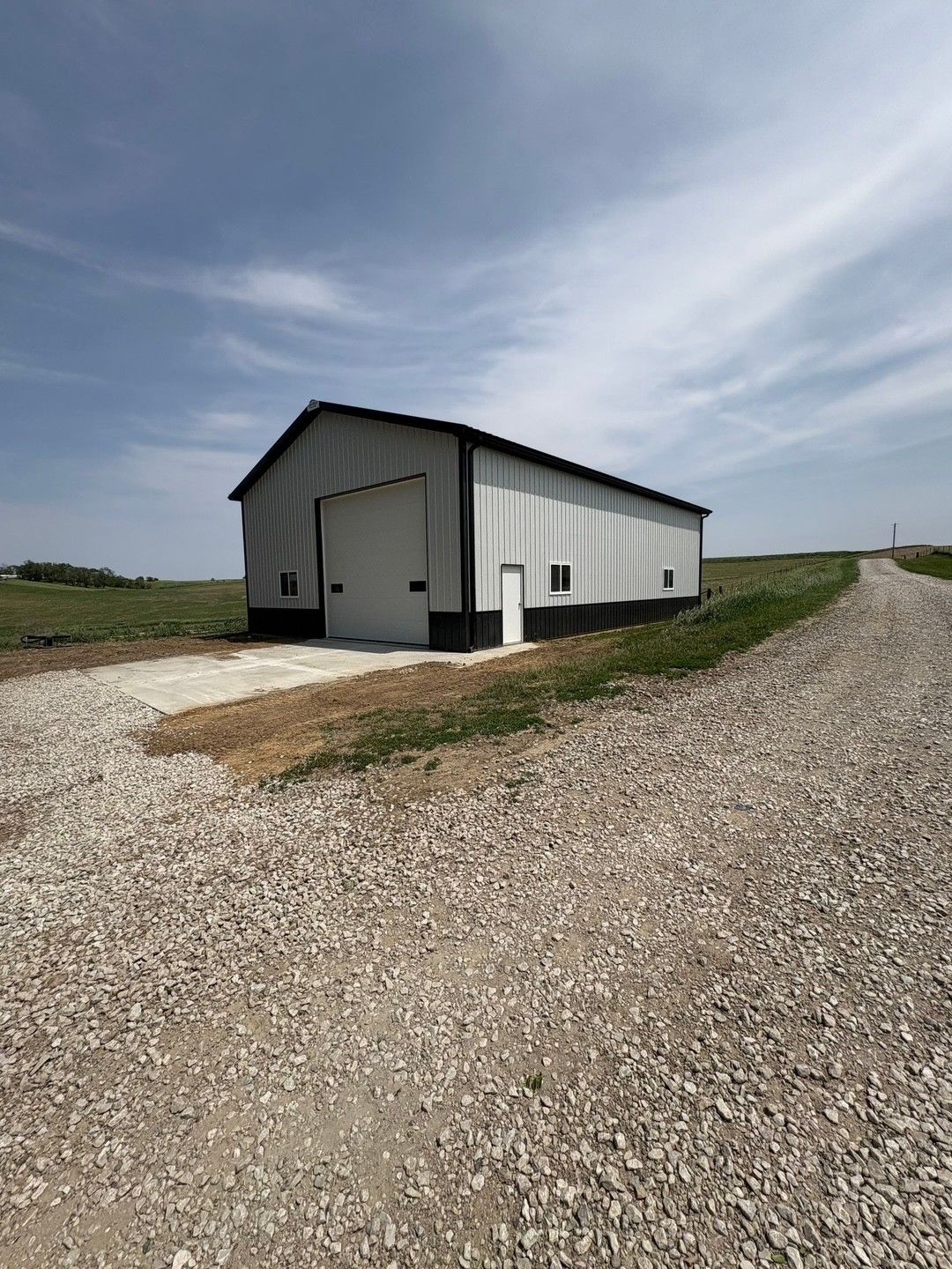 A metal barn with a large garage door on a gravel road under a cloudy sky.