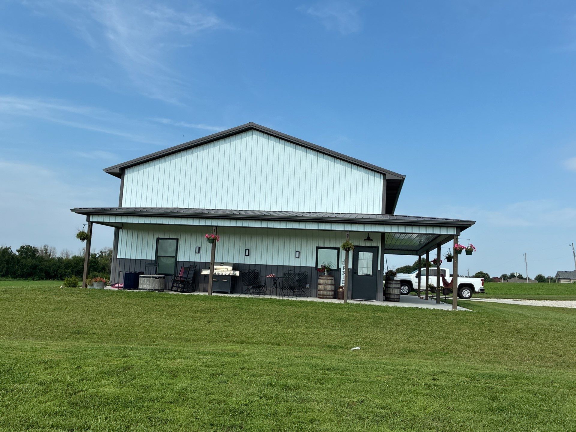 Two-story light blue building with a porch, parked white truck, and green grass against a blue sky.