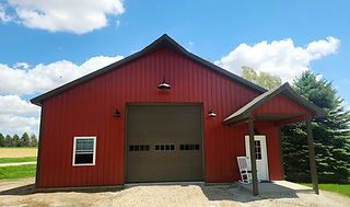 Metal building with brown roof and trim, a garage door, and a covered porch.