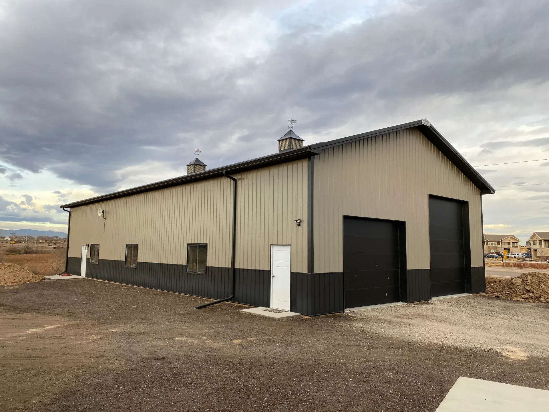 Tan and black metal building with two garage doors under a cloudy sky.