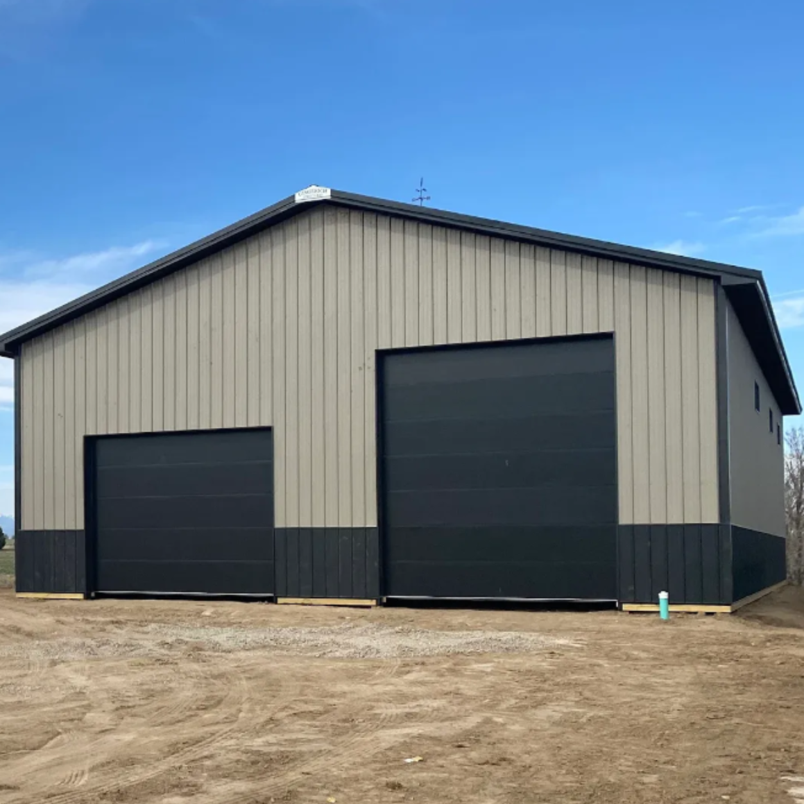 Tan and black metal building with two large garage doors against a blue sky.