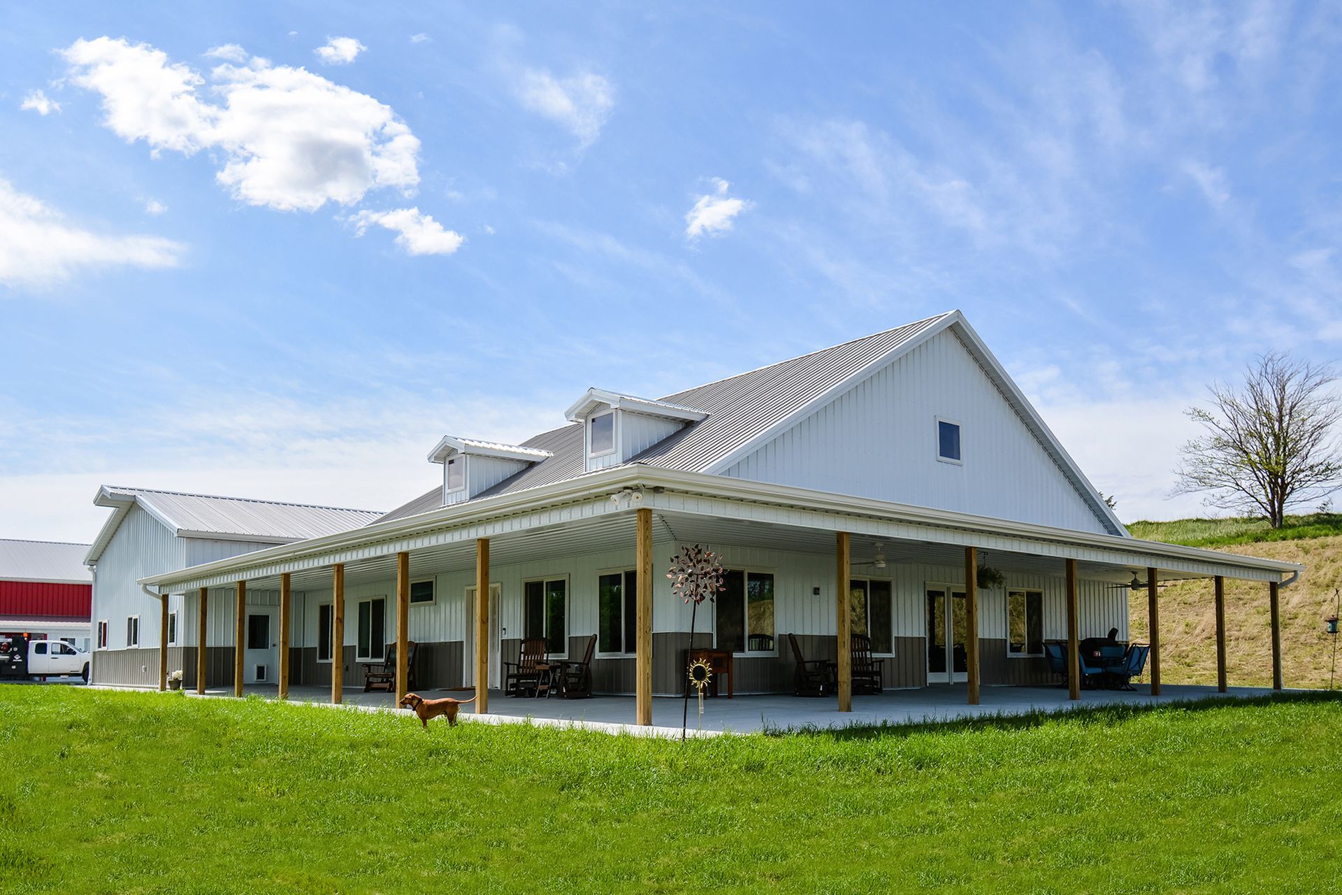 White farmhouse with large porch on a green lawn, against a blue sky with some clouds.